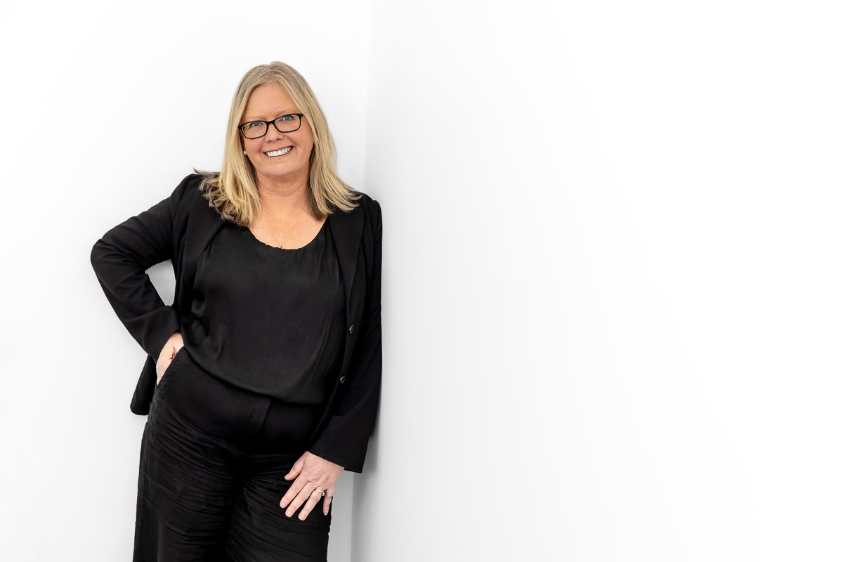 Middle aged woman with blonde hair leaning on white wall