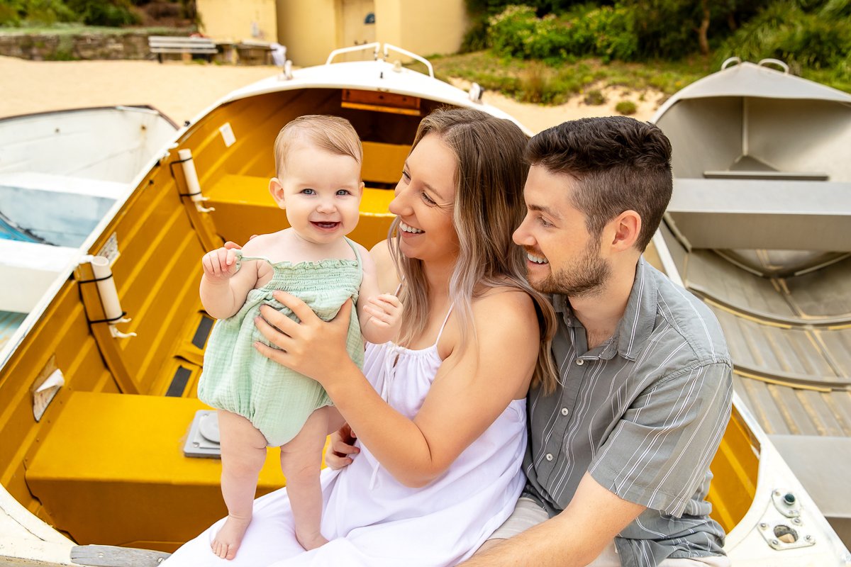 A young family cuddling sitting on one of the boats at Coogee Beach in the morning light