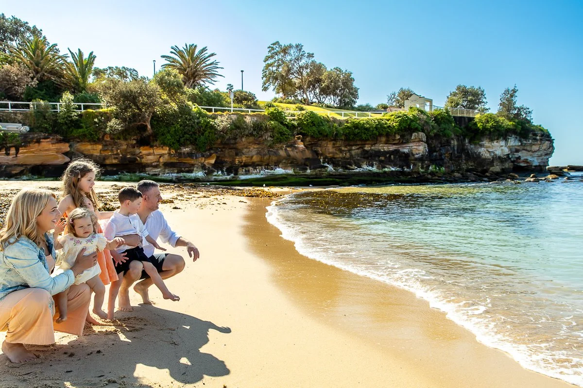 A young family crouched on the waters edge at Coogee Beach in the morning looking out at the gorgeous ocean.