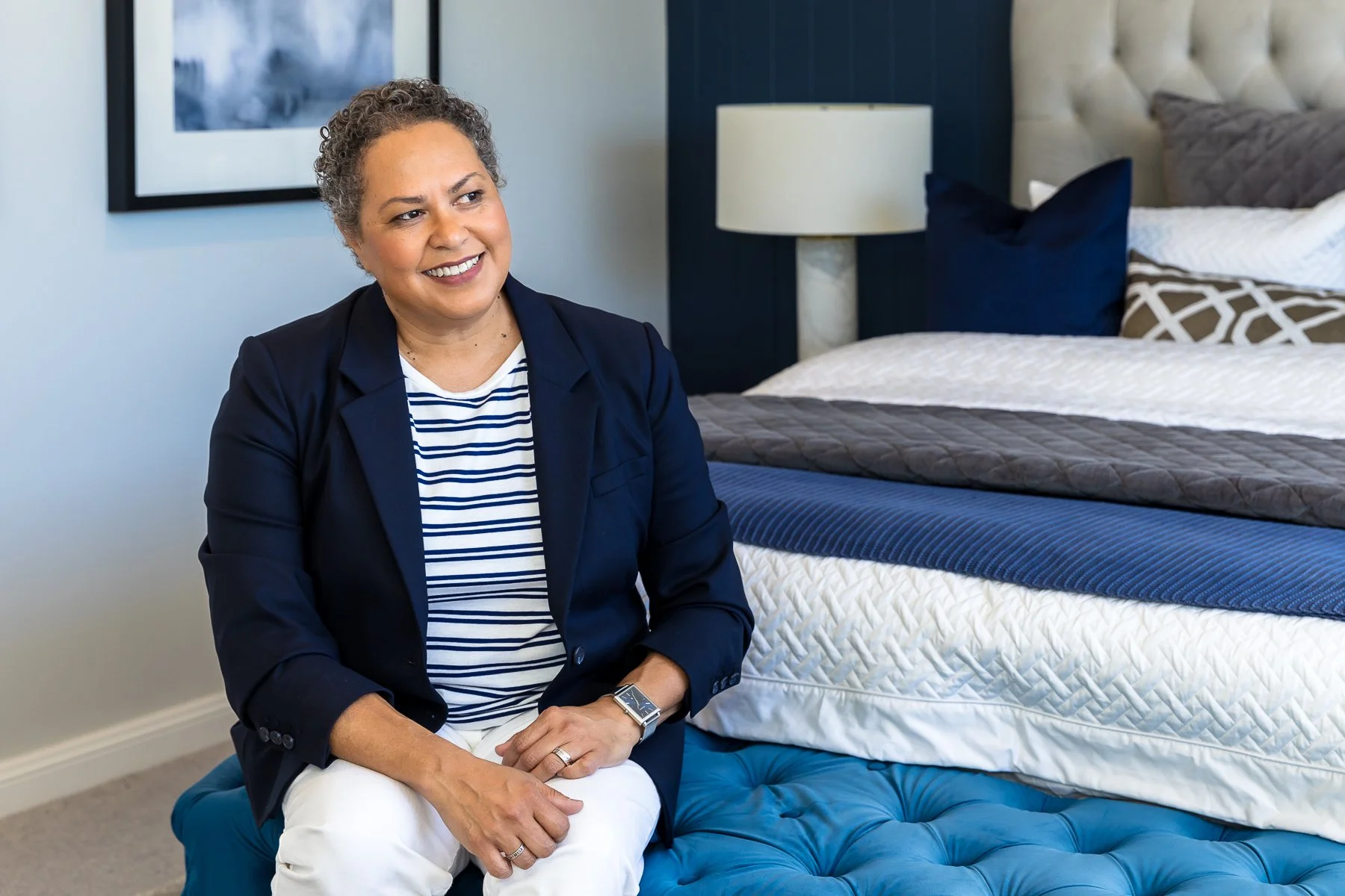 A woman sitting on an ottoman at the end of a bed in a stunning navy bedroom looking off to the side during a personal branding shoot in the Hills District of Sydney.