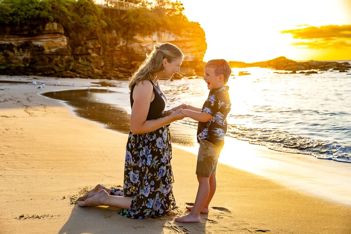 A mother on her knees, playing with her son in the golden hour light at Coogee Beach in Sydney for their outdoor family photoshoot.