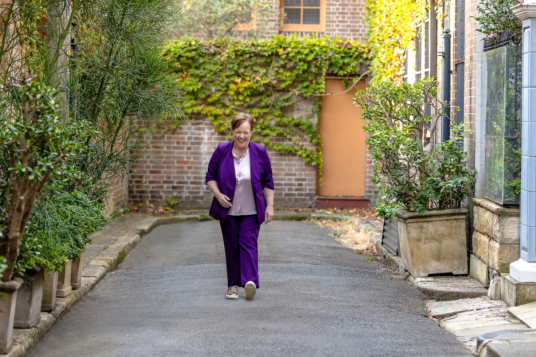 A woman in a purple suit walking and laughing, comfortable in front of the camera during her branding photoshoot in Sydney City.