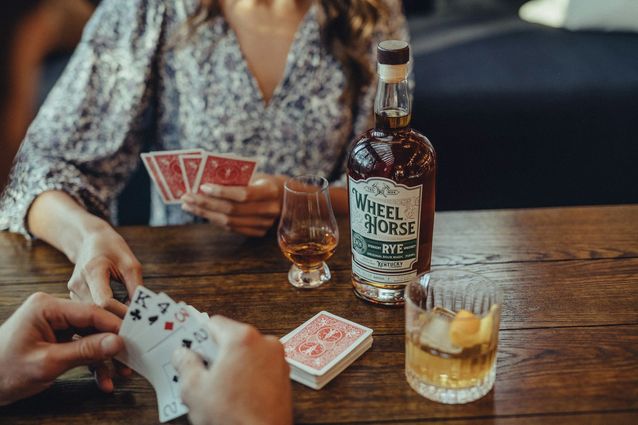 Two people playing cards with a glass a whiskey.