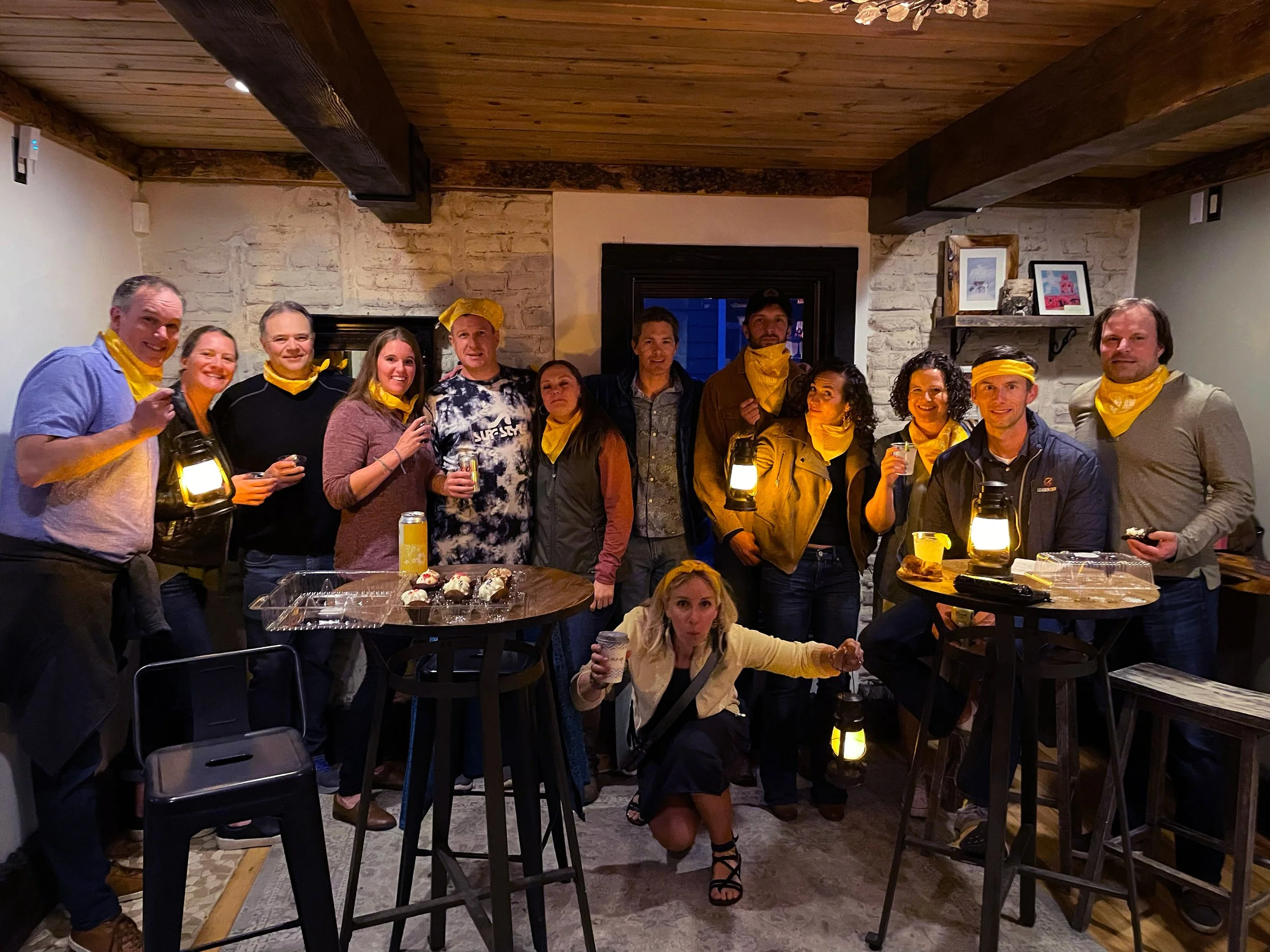 Group wearing gold bandanas holding lanterns around a table.