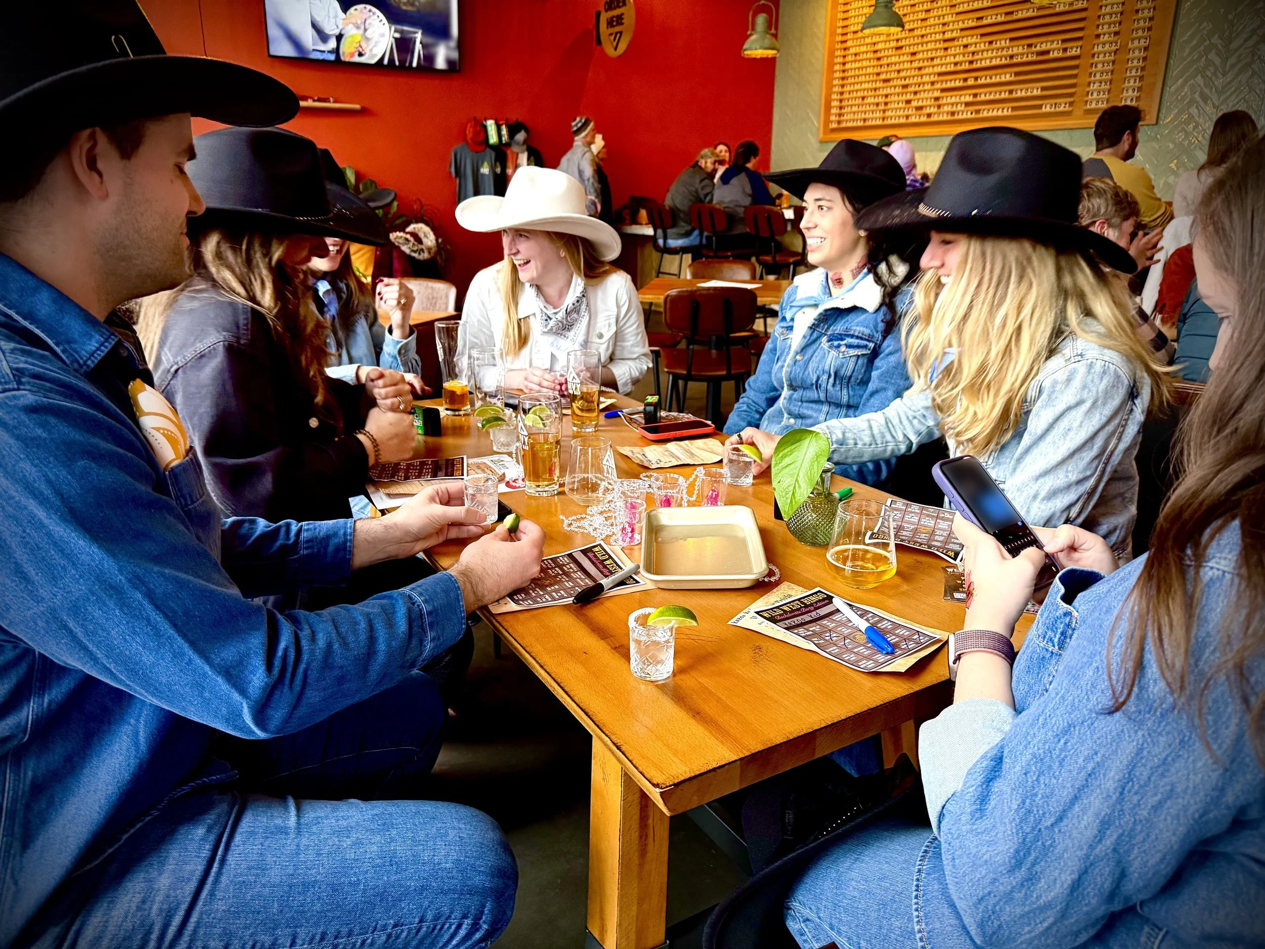 A group dressed in fun western wear having fun around a table.