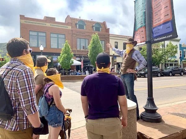 A tour guide wearing a bandana directs a group toward an old building.