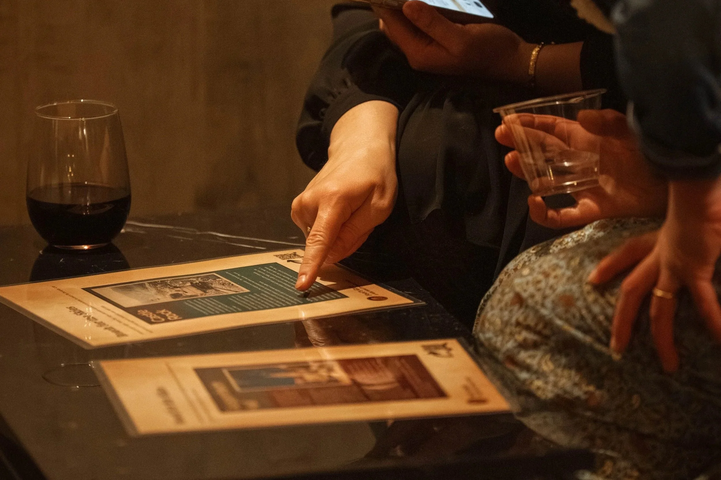 A person points at a laminated clue sitting next to a wine glass.