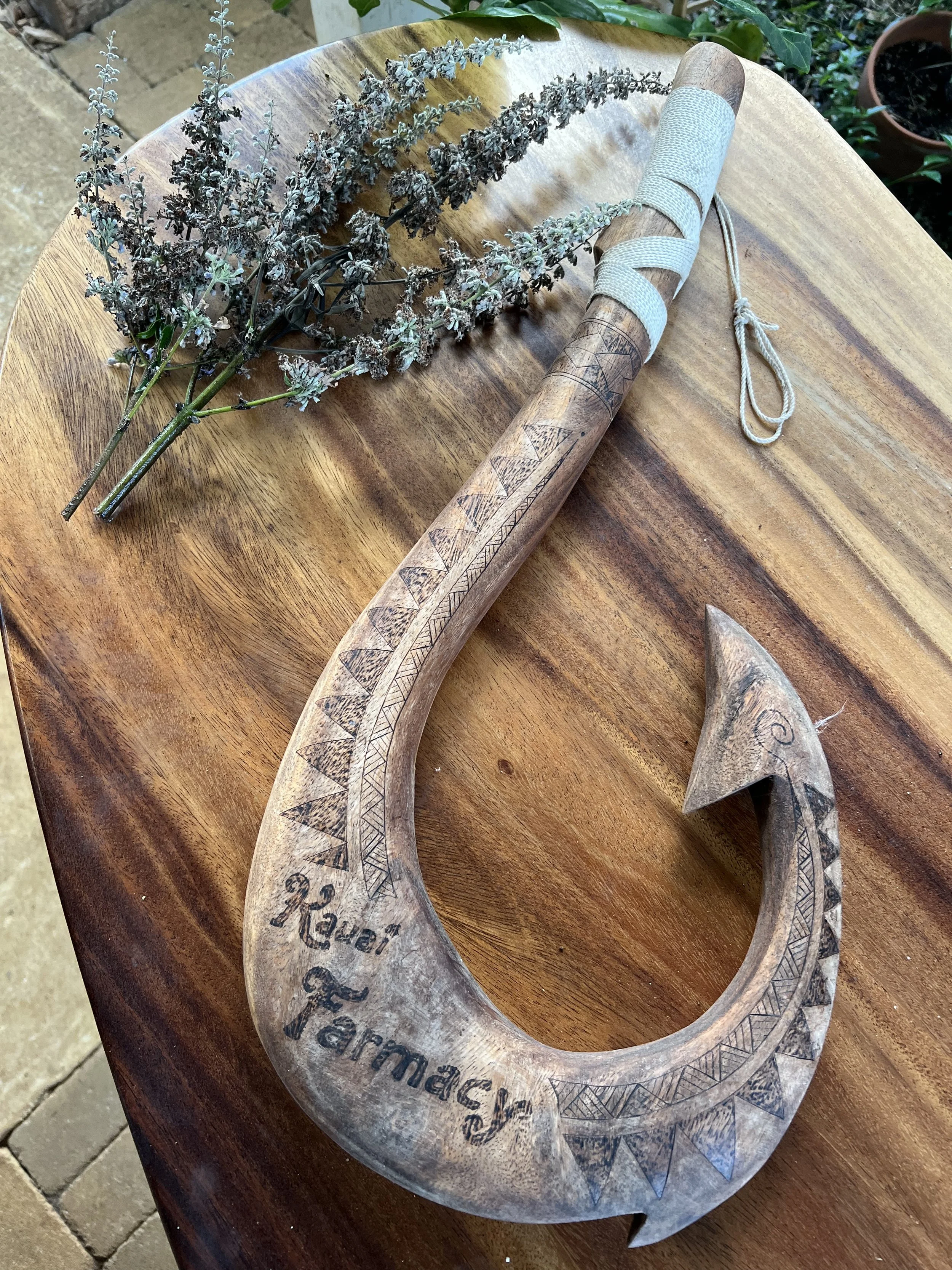 A carved wooden hook with the words 'Be a Farmer' written on it, resting on a wooden surface with sprigs of dried lavender nearby.
