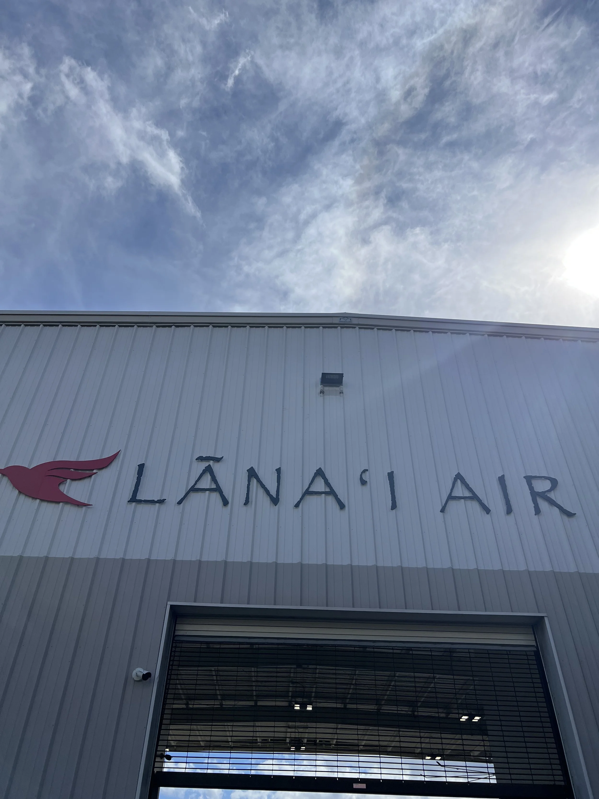 Exterior view of a building with the sign 'LANAIR' and an abstract wing logo, under a partly cloudy sky.