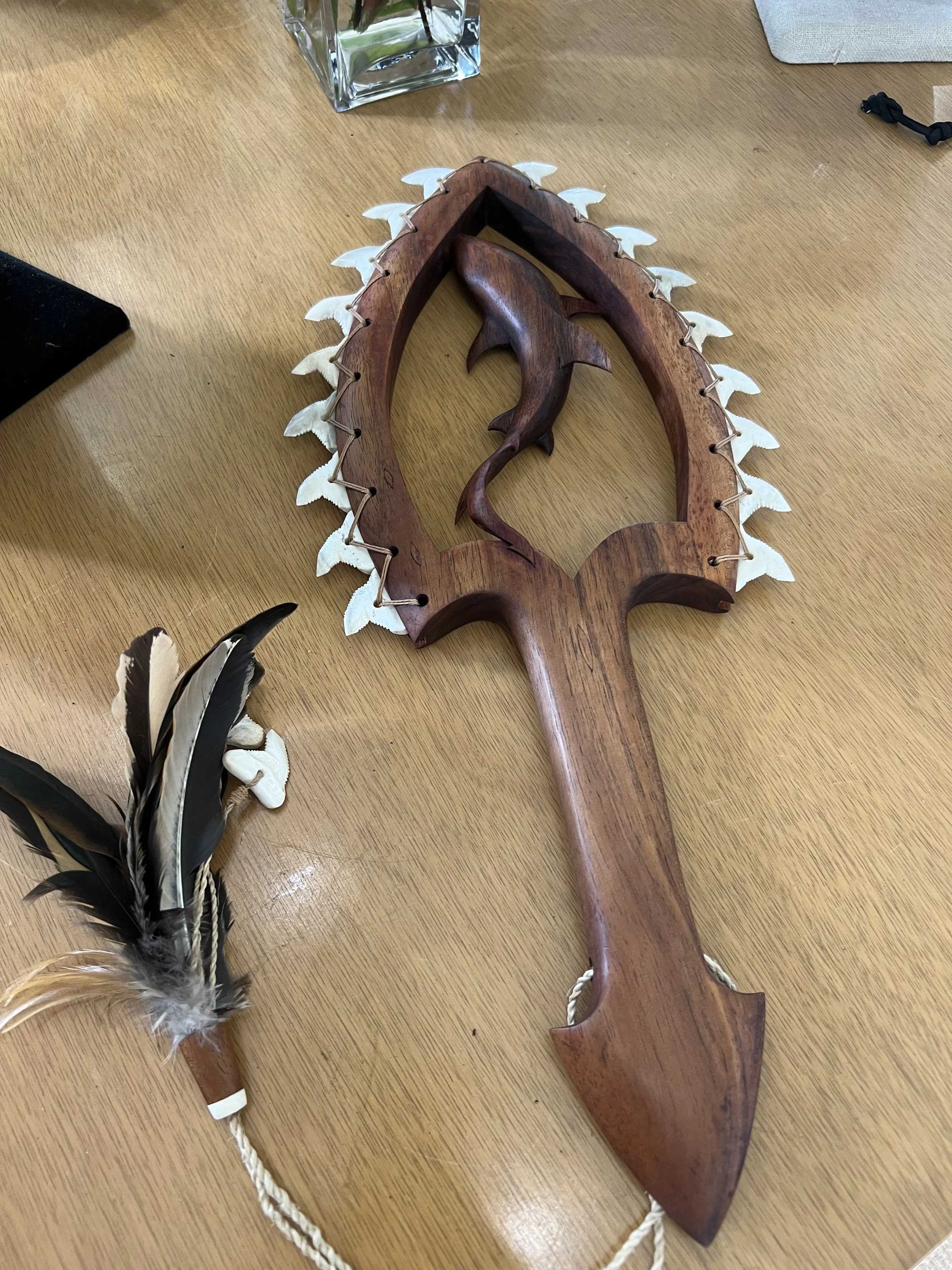 A wooden handcrafted dreamcatcher with a carved fish in the center, surrounded by a frame decorated with white feathers, resting on a wooden surface.