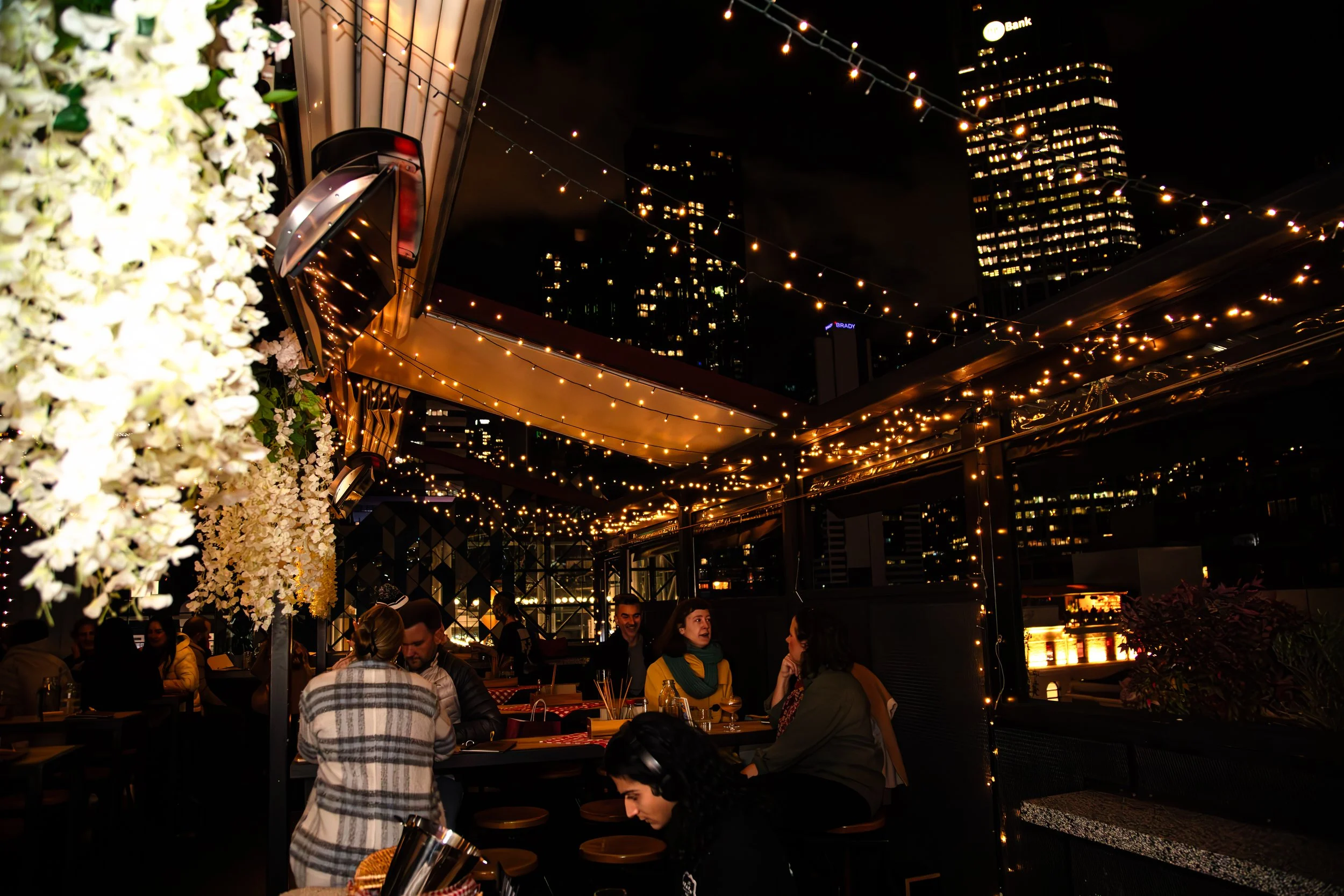 Guests enjoying a winter evening at Goldilocks Rooftop Bar in Melbourne CBD, with rooftop seating, city views and warm lights.
