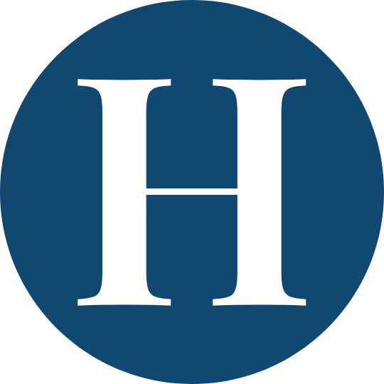 A circular emblem with a dark blue background and a large white letter H in the center.