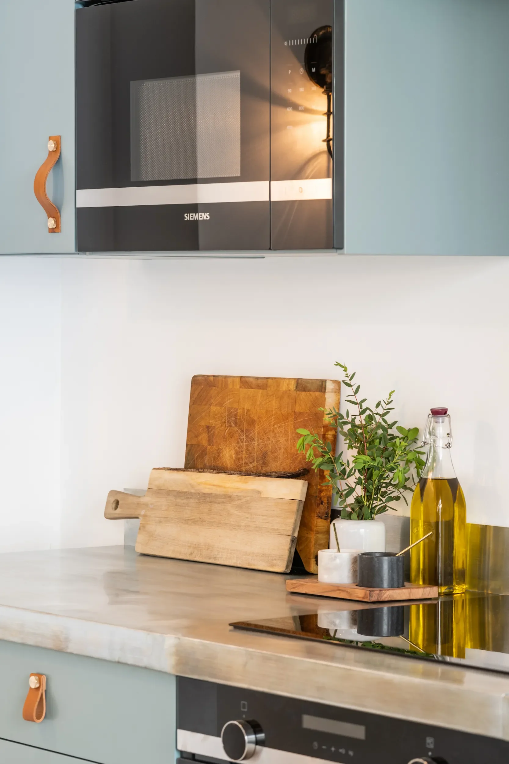 Kitchen counter with wooden cutting boards, a small potted plant, glass bottles of oil, and a modern oven in the background.