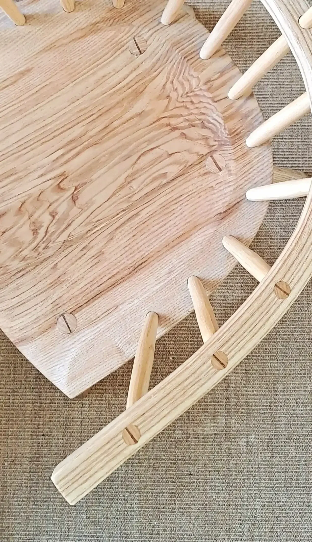 Close-up view of a wooden chair with rounded vertical slats and a wood seat, shown from underneath with a visible screw and wood grain pattern.