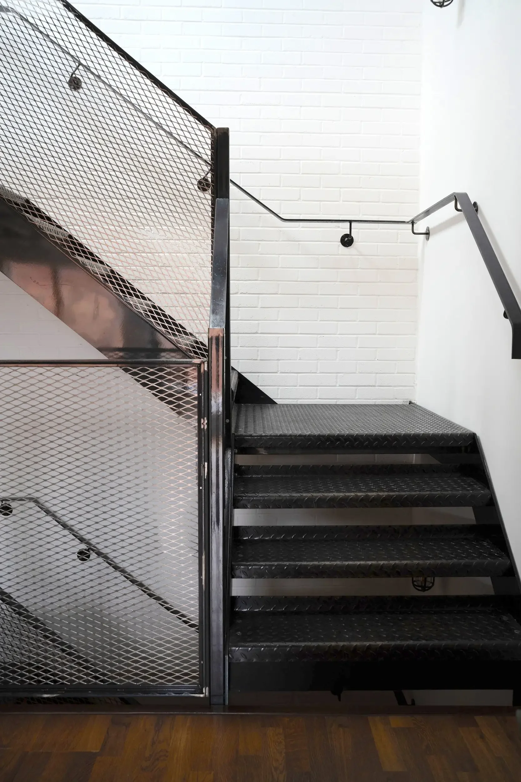 Indoor staircase with black steps, a black metal handrail, and a white brick wall background.