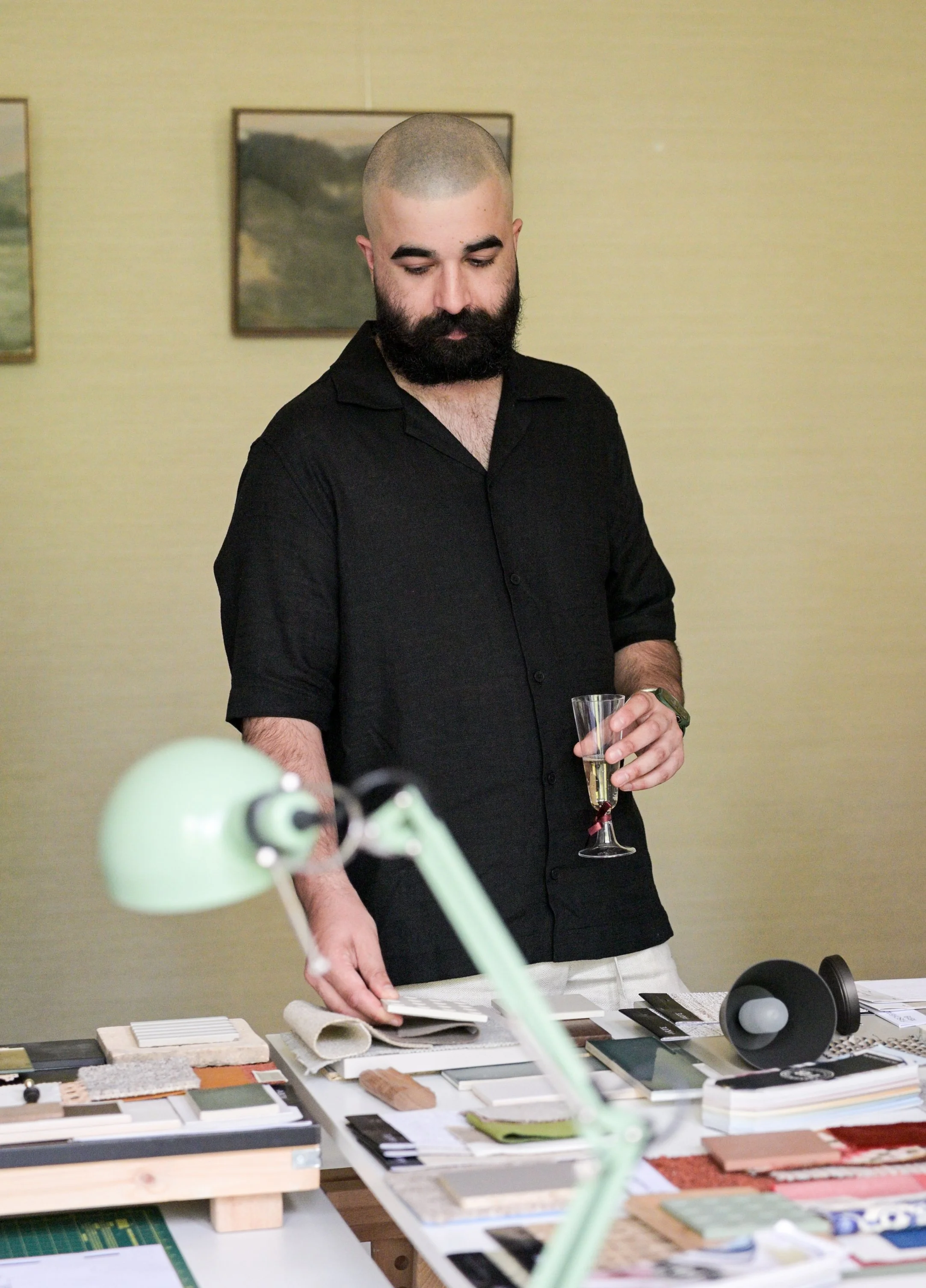 Table full of material samples. Man holding a glass of champagne.