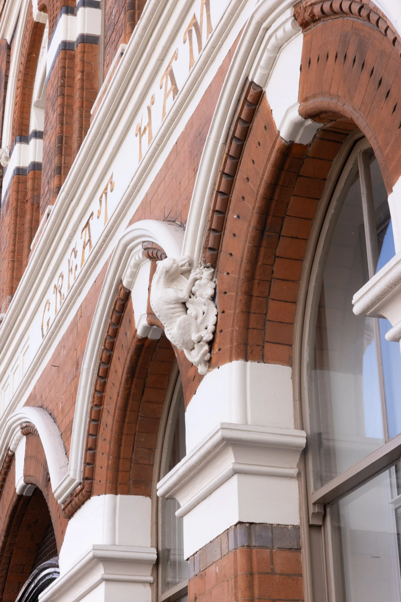 Close-up of a historic building's facade showing decorative white architectural details, two arched windows with white frames, and red brickwork.