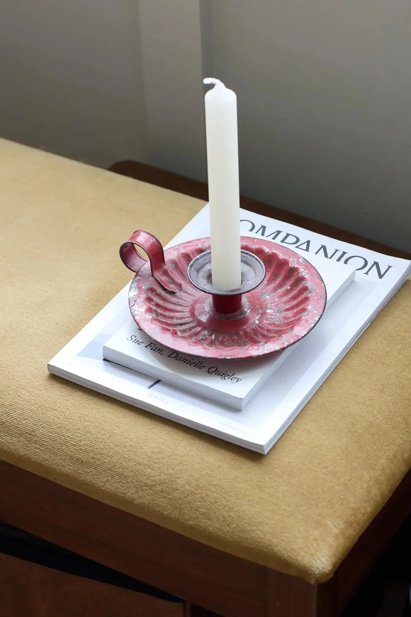 White candle in a glass holder on a decorative pink dish, placed on top of a book titled 'COMMAND' on a beige table.
