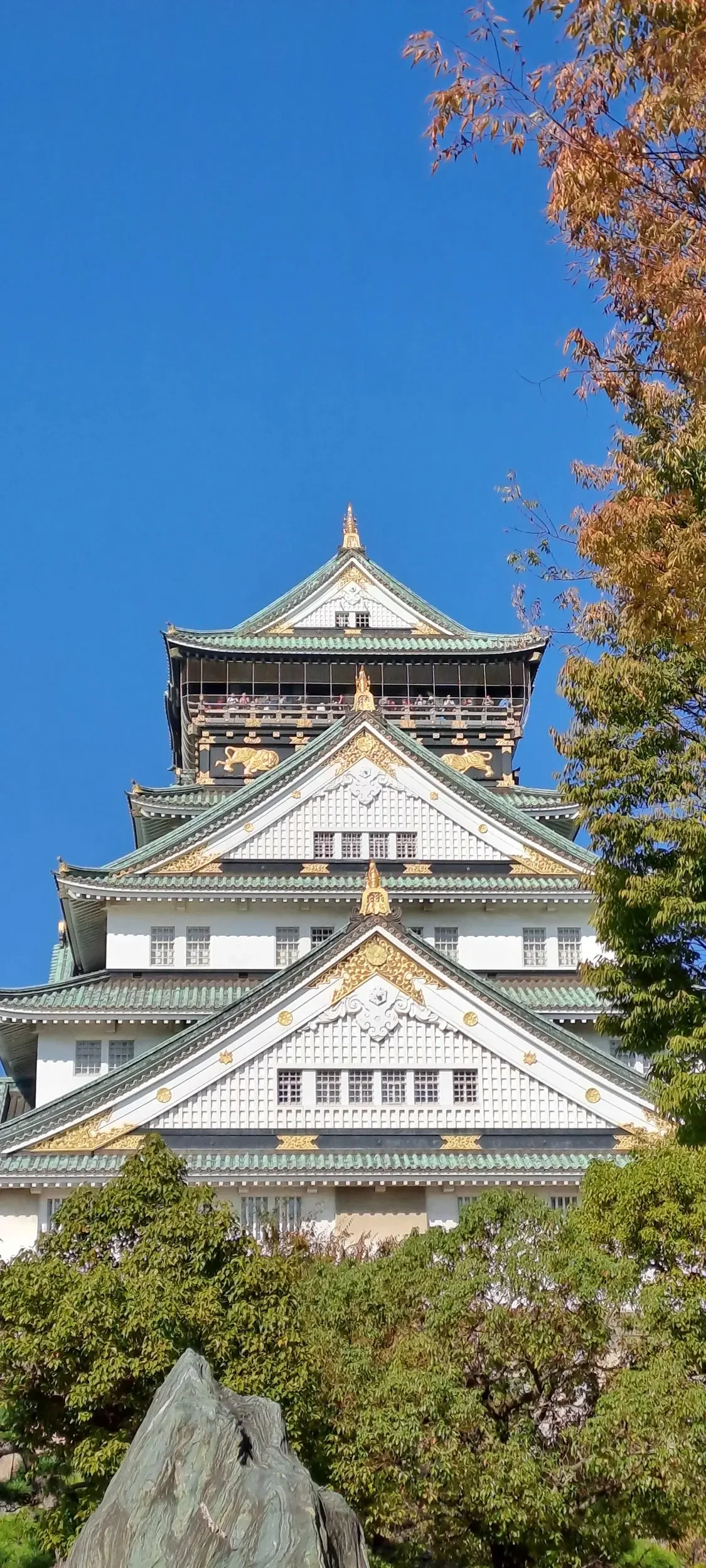 Traitional Japanese building with white and gold details. Grey and green roof tiles.