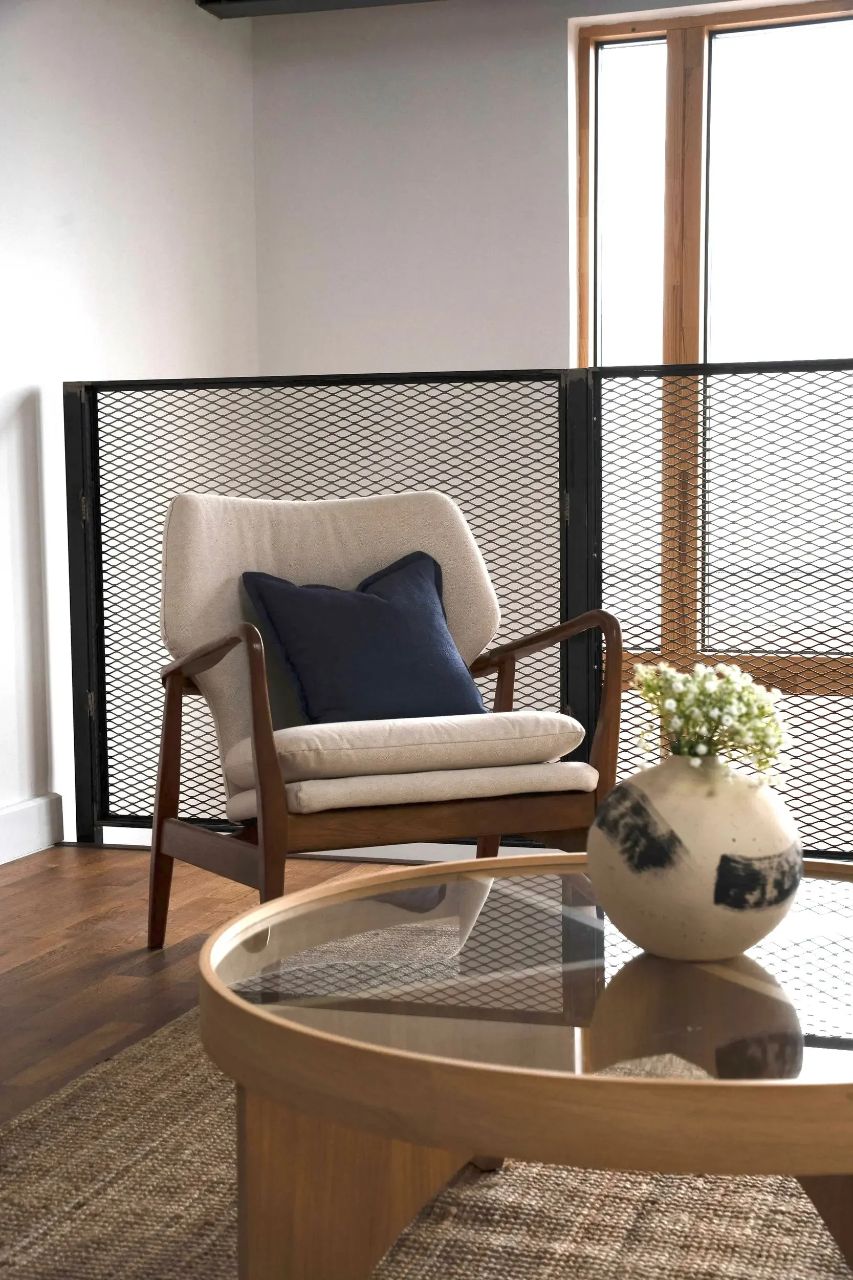 Dark stained armchair and a round oak and glass coffee table. Large neutral woven rug. Styled by San Stae Interior Design and Art Studio.