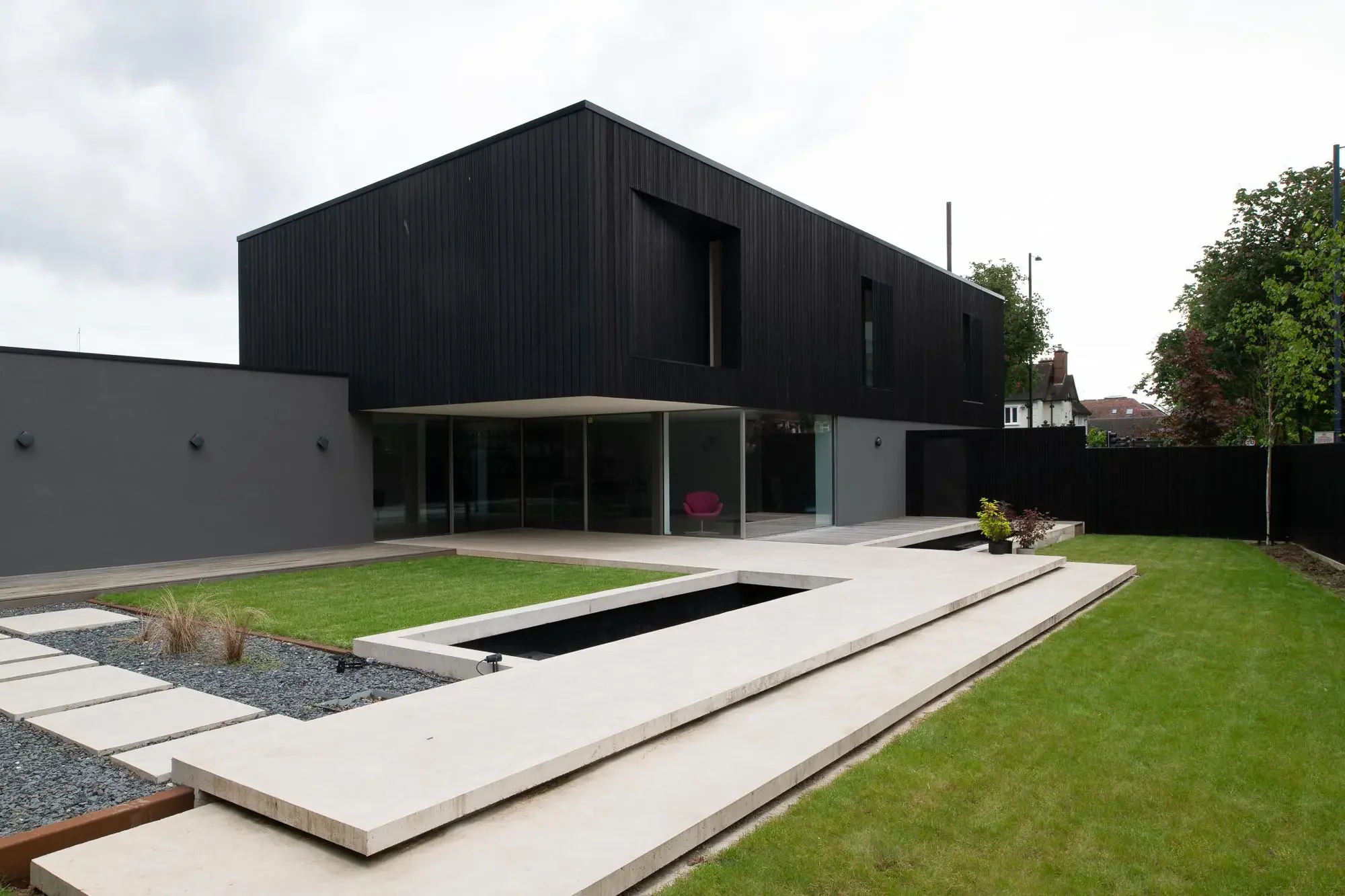 Modern black and gray house with landscaped yard, concrete steps, and minimalist garden.