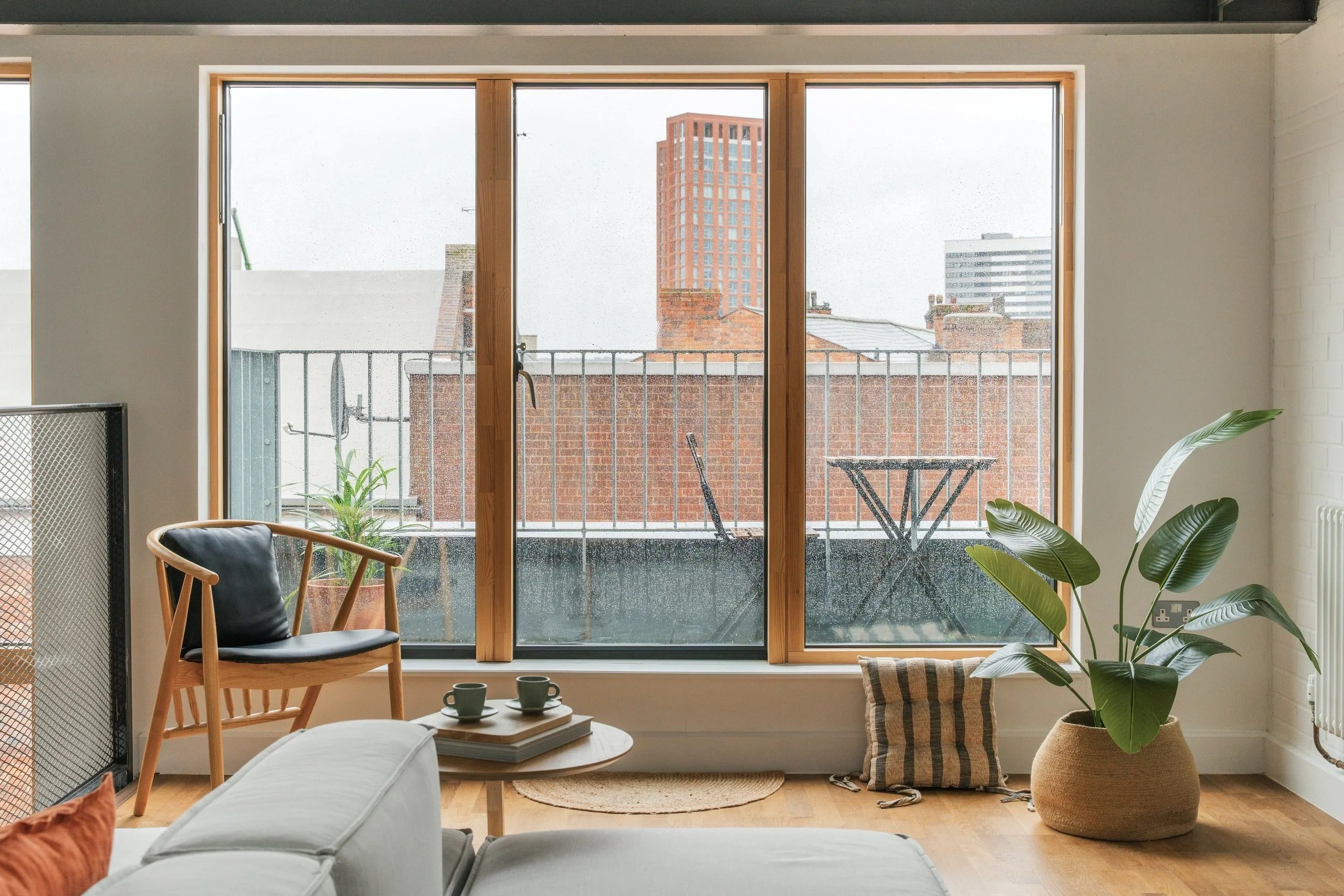 Top floor of the Alben Works townhouse. Seating area with a grey sofa and an oak armchair. Overlooking the surrounding buildings. Small seating area on the exterior balcony.
