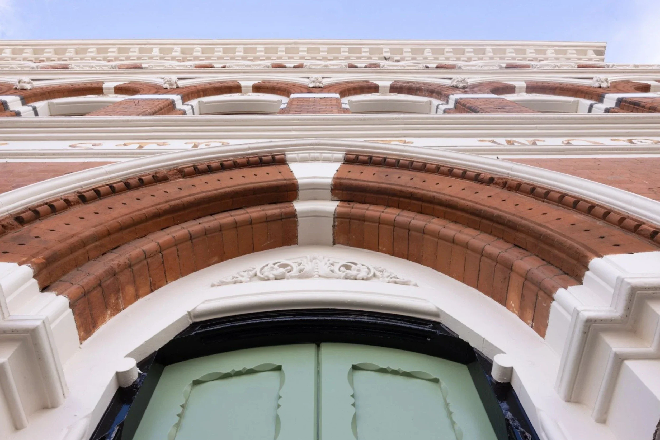 Close-up view of the ornate architectural details of a historic building, including decorative brickwork, white embellished moldings, and a green door with intricate designs.