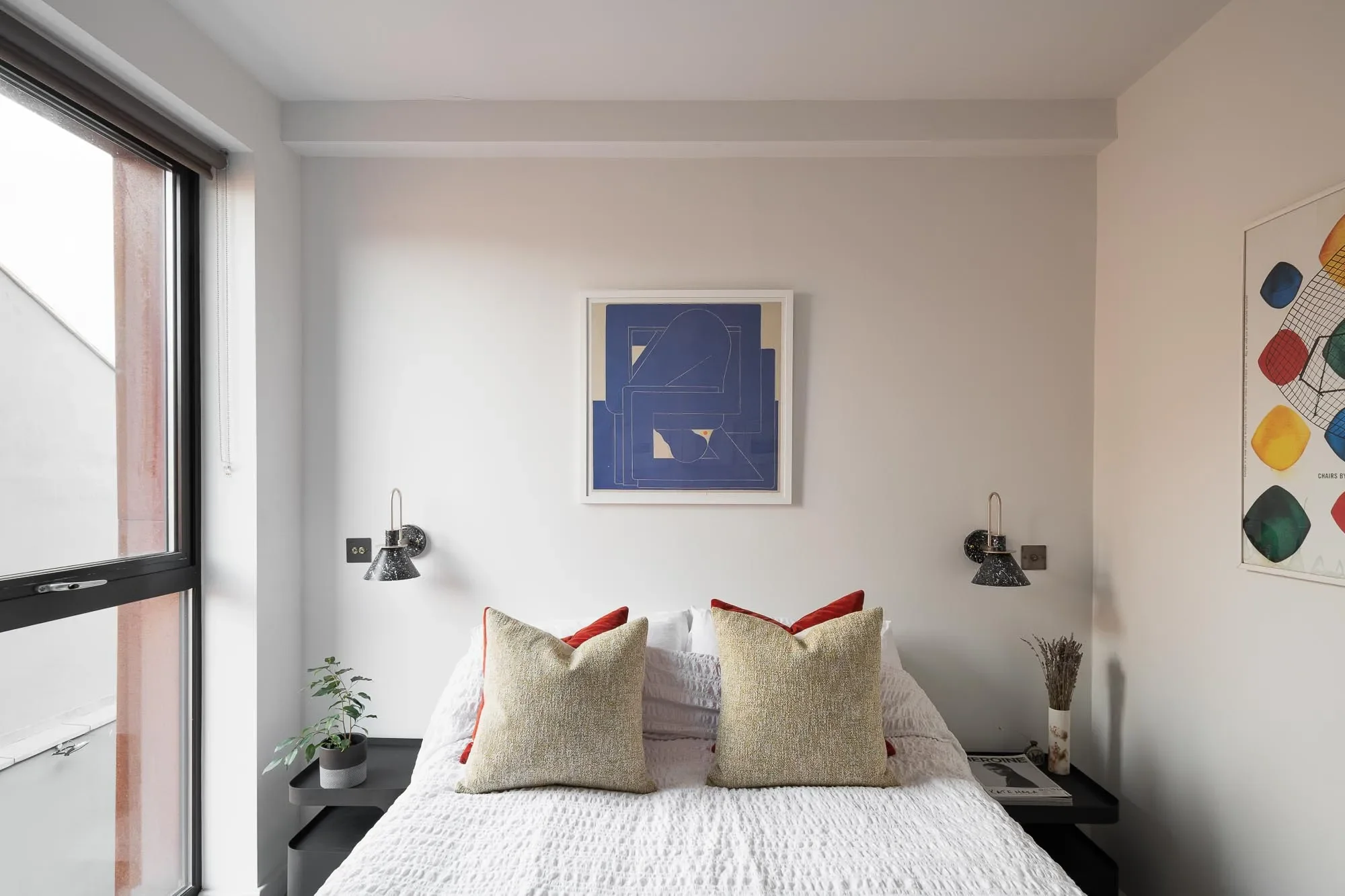 Modern bedroom with a bed, pillows, side tables, wall art, and a window.