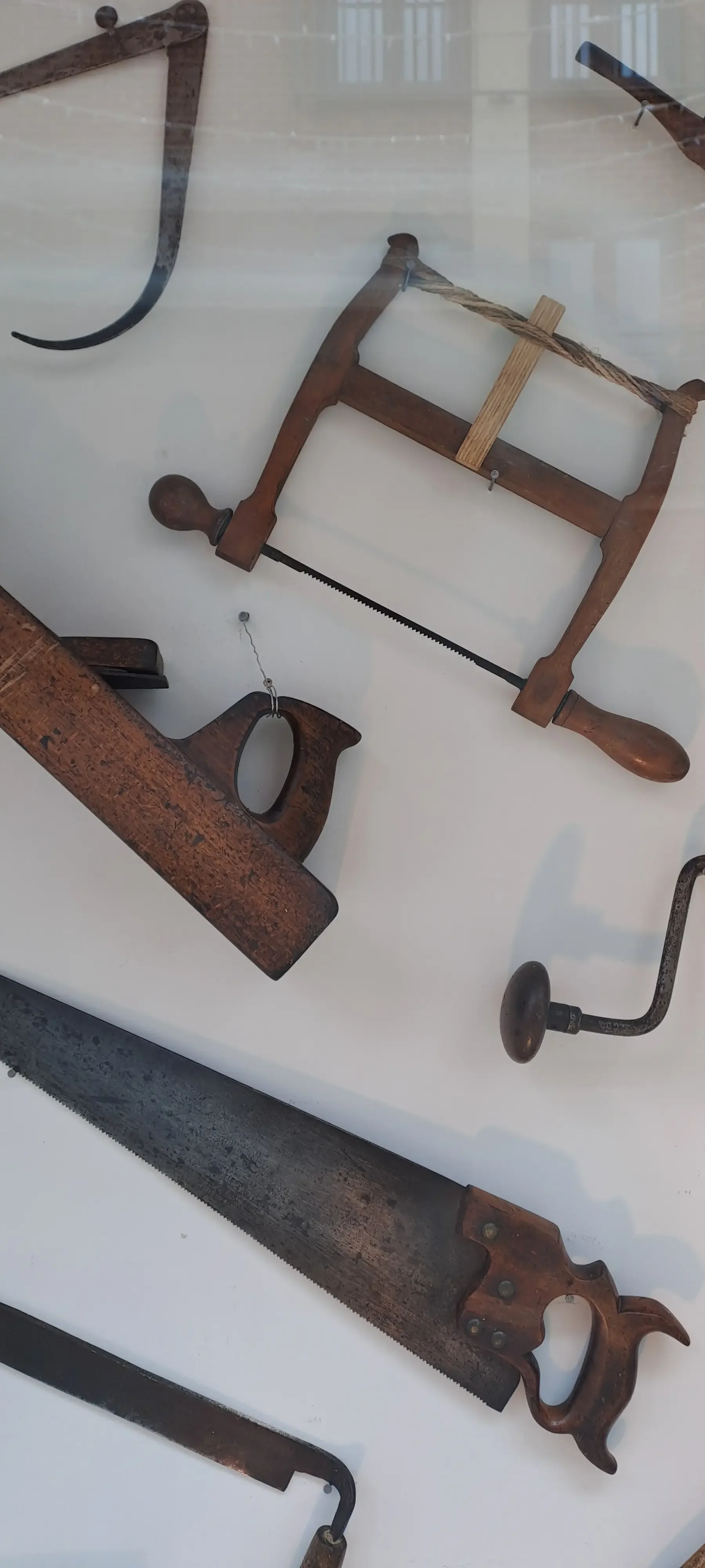 Collection of vintage hand saws and woodworking tools behind glass display.