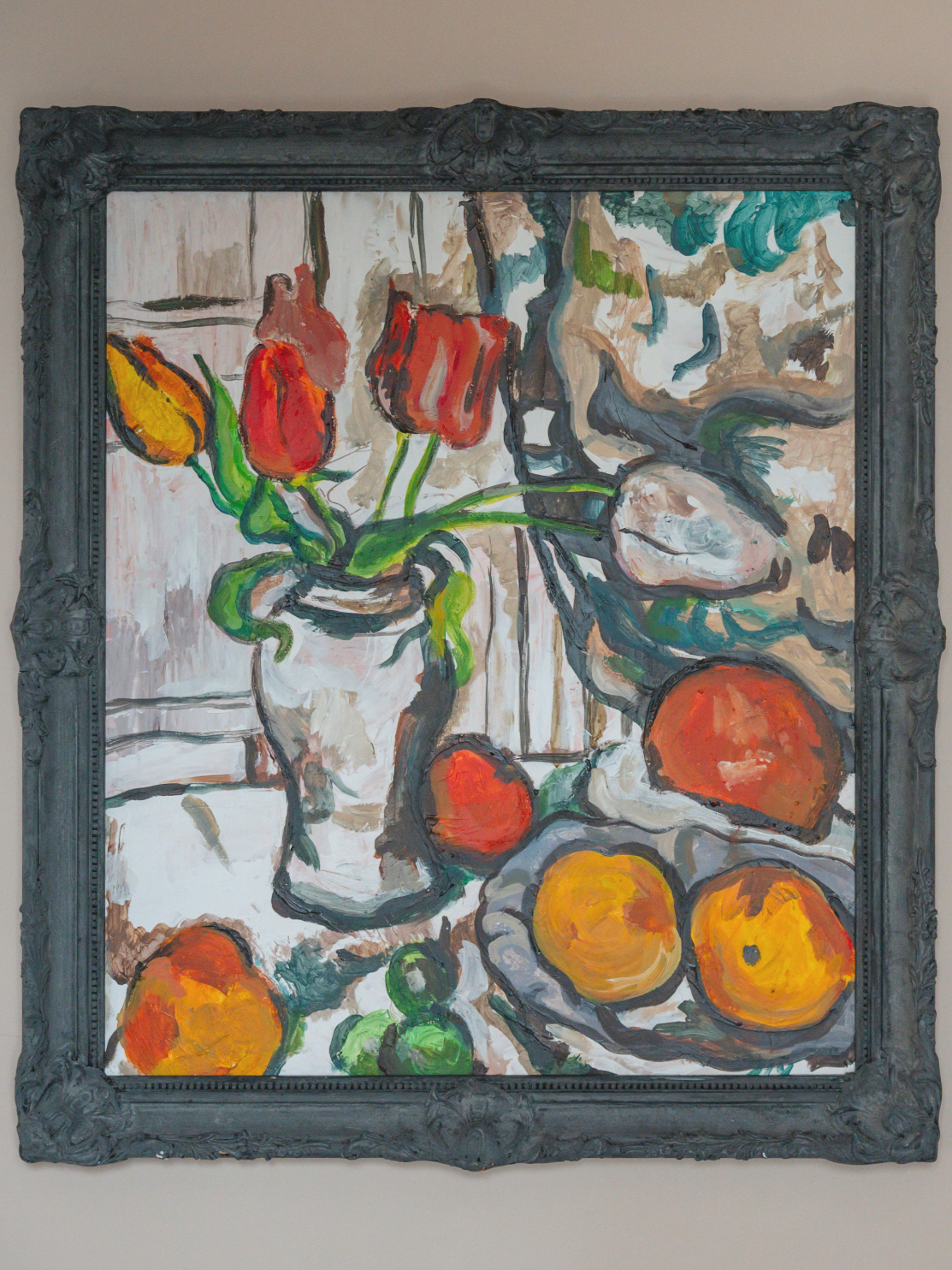 Oil painting of a still life with a vase of tulips and various fruits, in a decorative dark frame.
