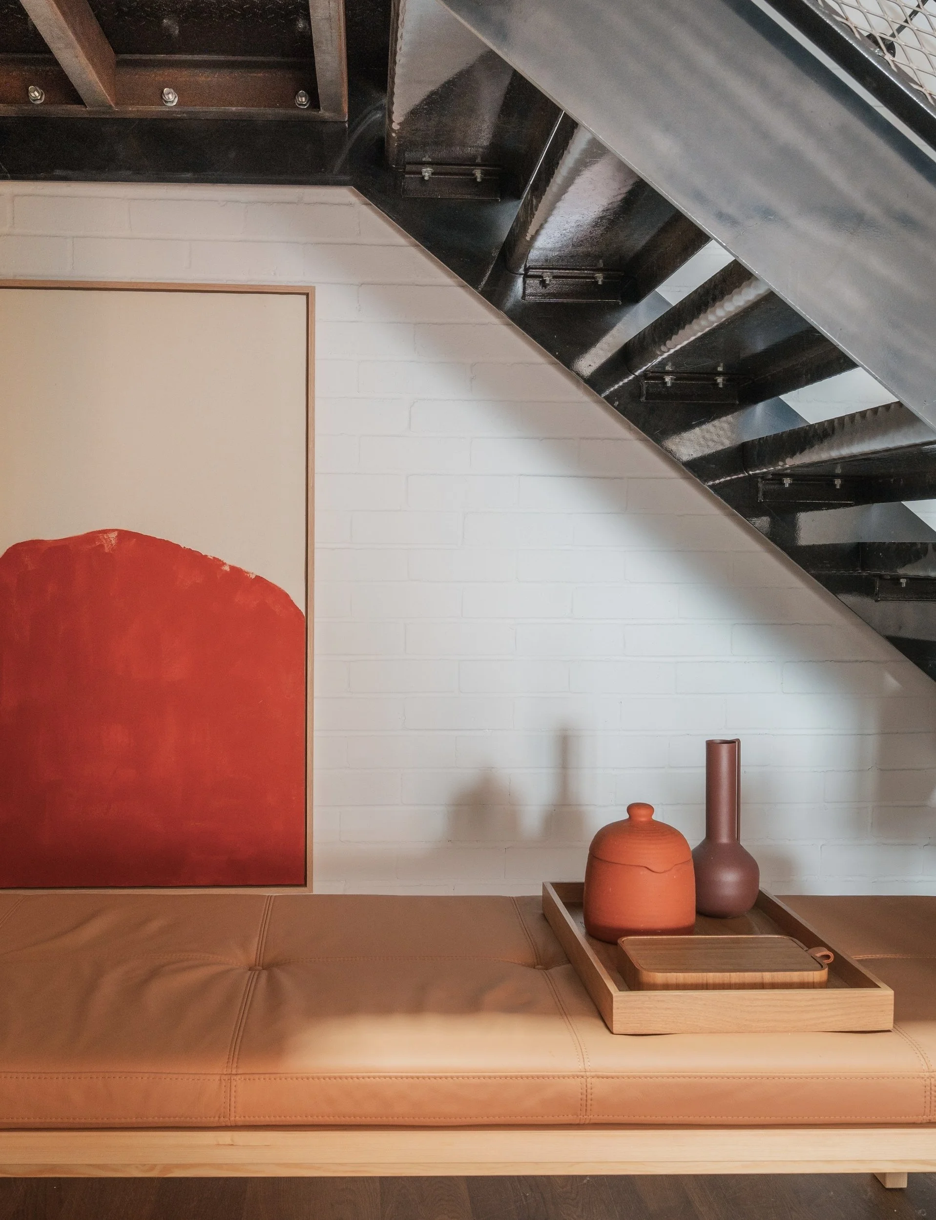 Industrial black metal staircase. Wooden bench with leather cushion. Tray full of ceramics. Orange and canvas artwork in a oak tray frame.