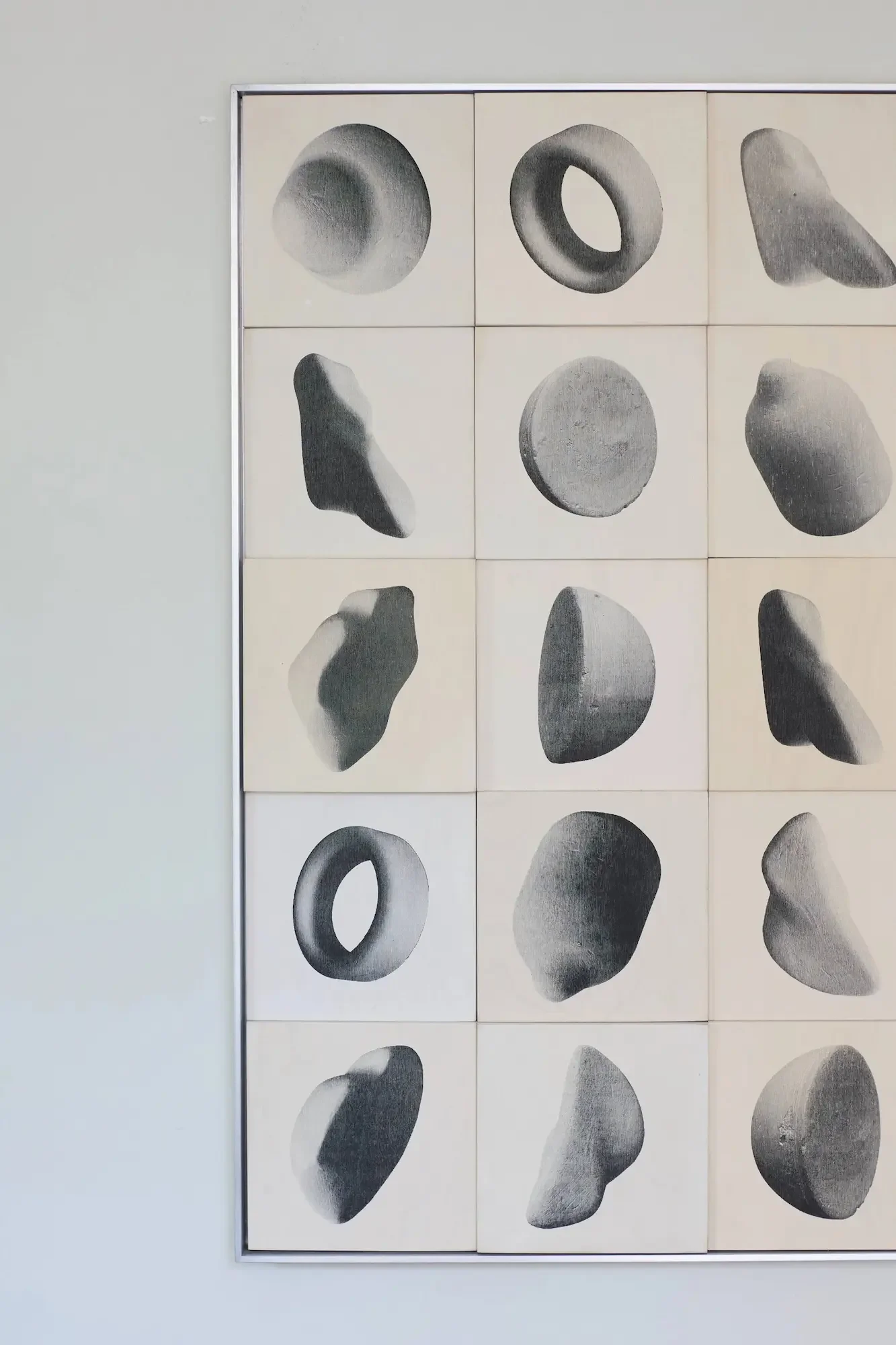 A framed display of nine black and white sketches of various stones and rocks arranged in a 3x3 grid on a white wall.
