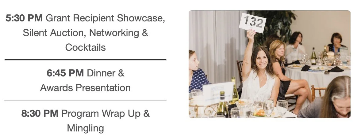 A woman at a dinner event holds up a sign with the number 132, smiling, with other attendees seated at tables in the background.