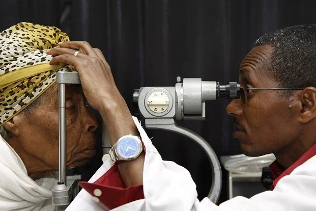 A doctor performing an eye examination on a woman using a slit lamp in a clinical setting.