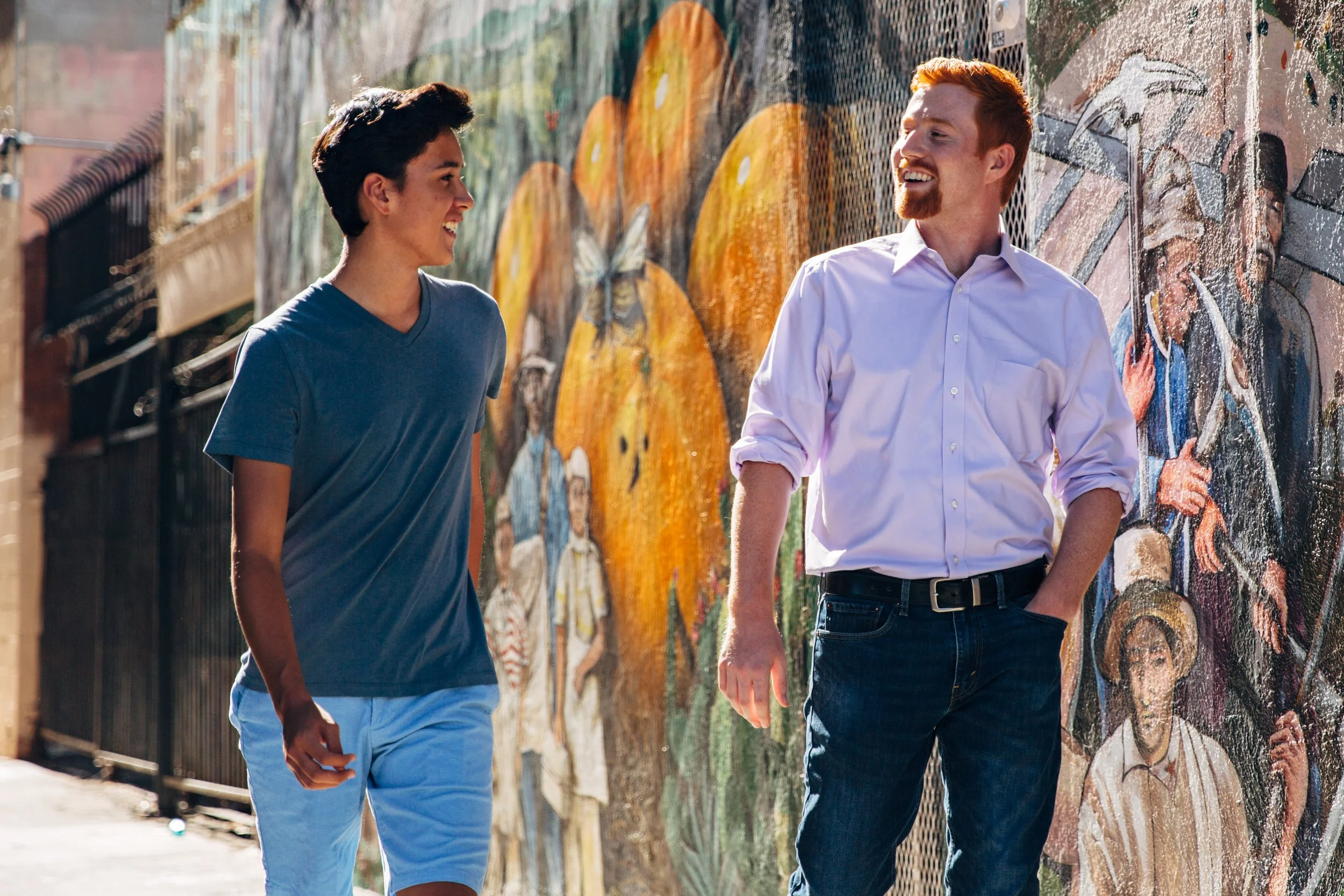 Two young men walking along a mural wall, smiling and engaging in conversation.