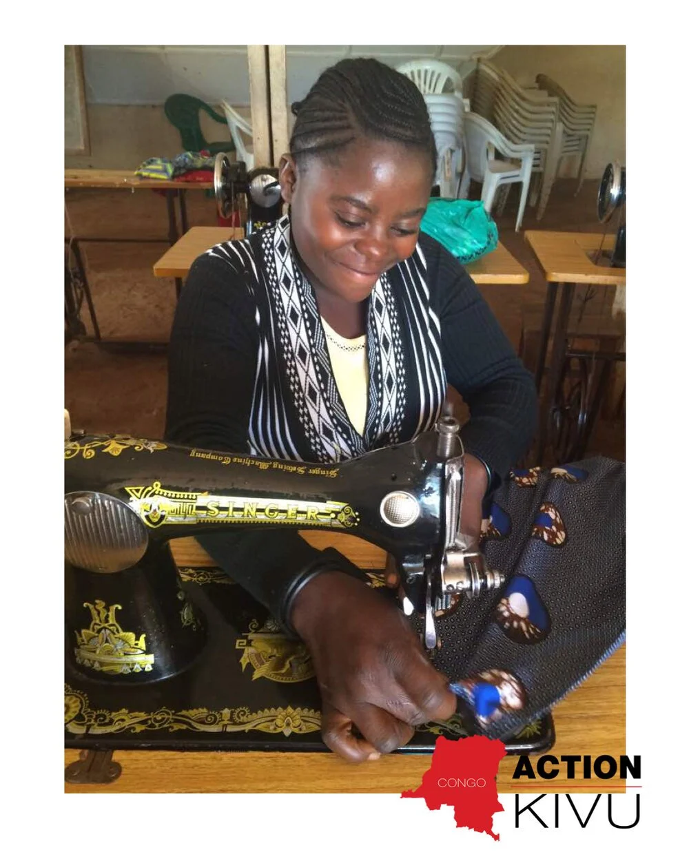 A woman operating a vintage Singer sewing machine, sewing fabric with butterfly patterns in a room with stacked plastic chairs and wooden furniture.