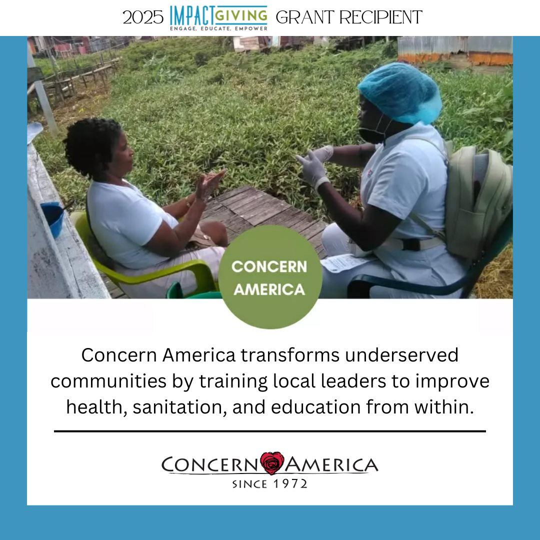 A woman wearing medical attire, including gloves, a face mask, and a hair cover, sitting outside at a table while speaking with a young girl in a white shirt. The background features green grass and plants, indicating an outdoor setting.