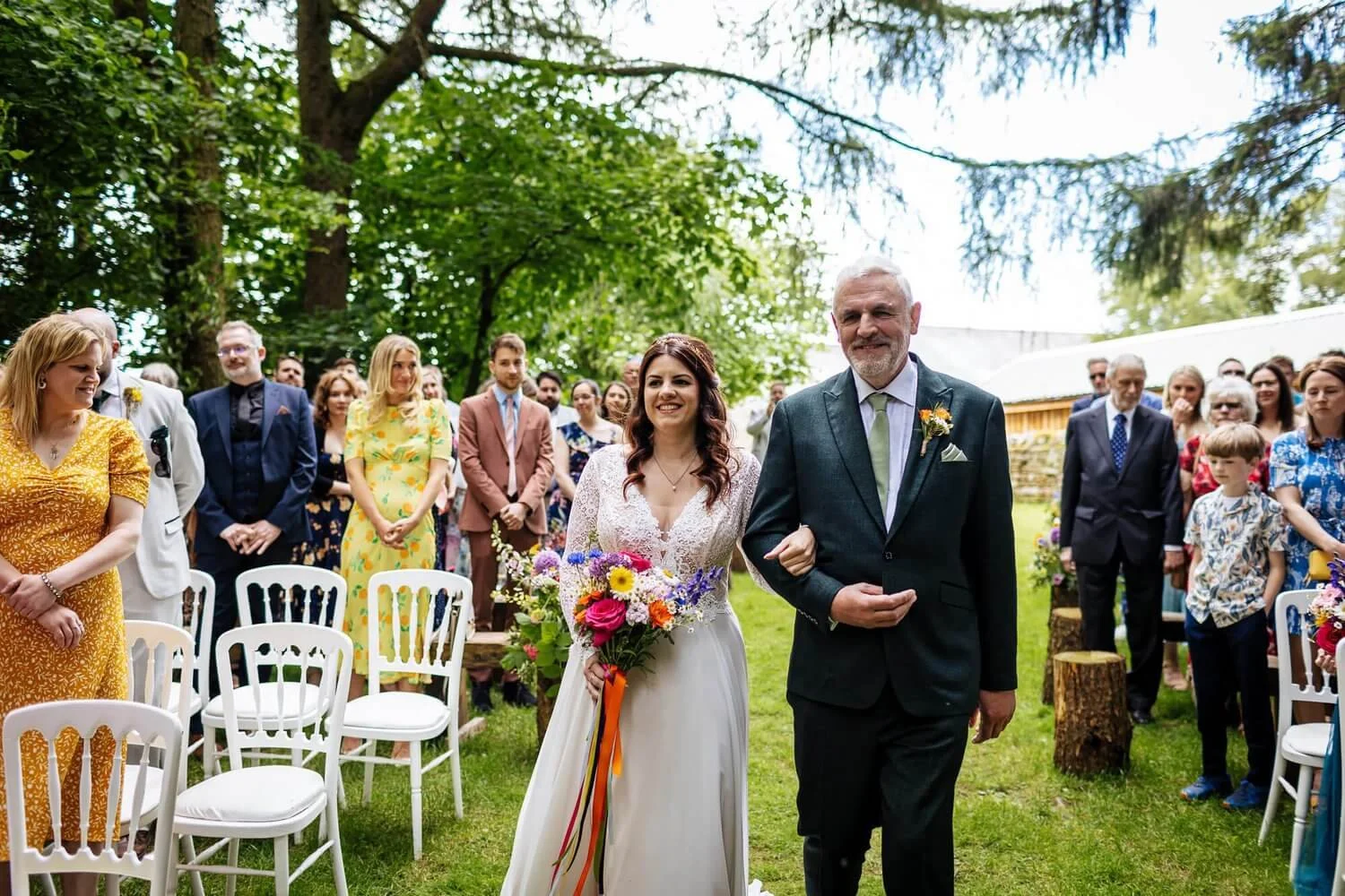 Bride walks down the aisle with her father in a non-religious, outdoor wedding ceremony at Lineham Farm, Leeds, West Yorkshire