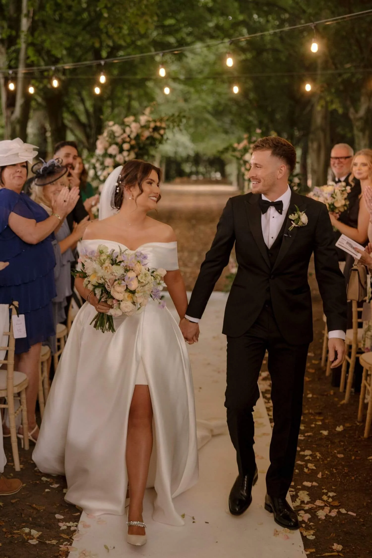 Bride  in a white wedding dress and groom in a tux, hold hands in the aisle in the woods of Saltmarshe Hall, Howden after their celebrant ceremony