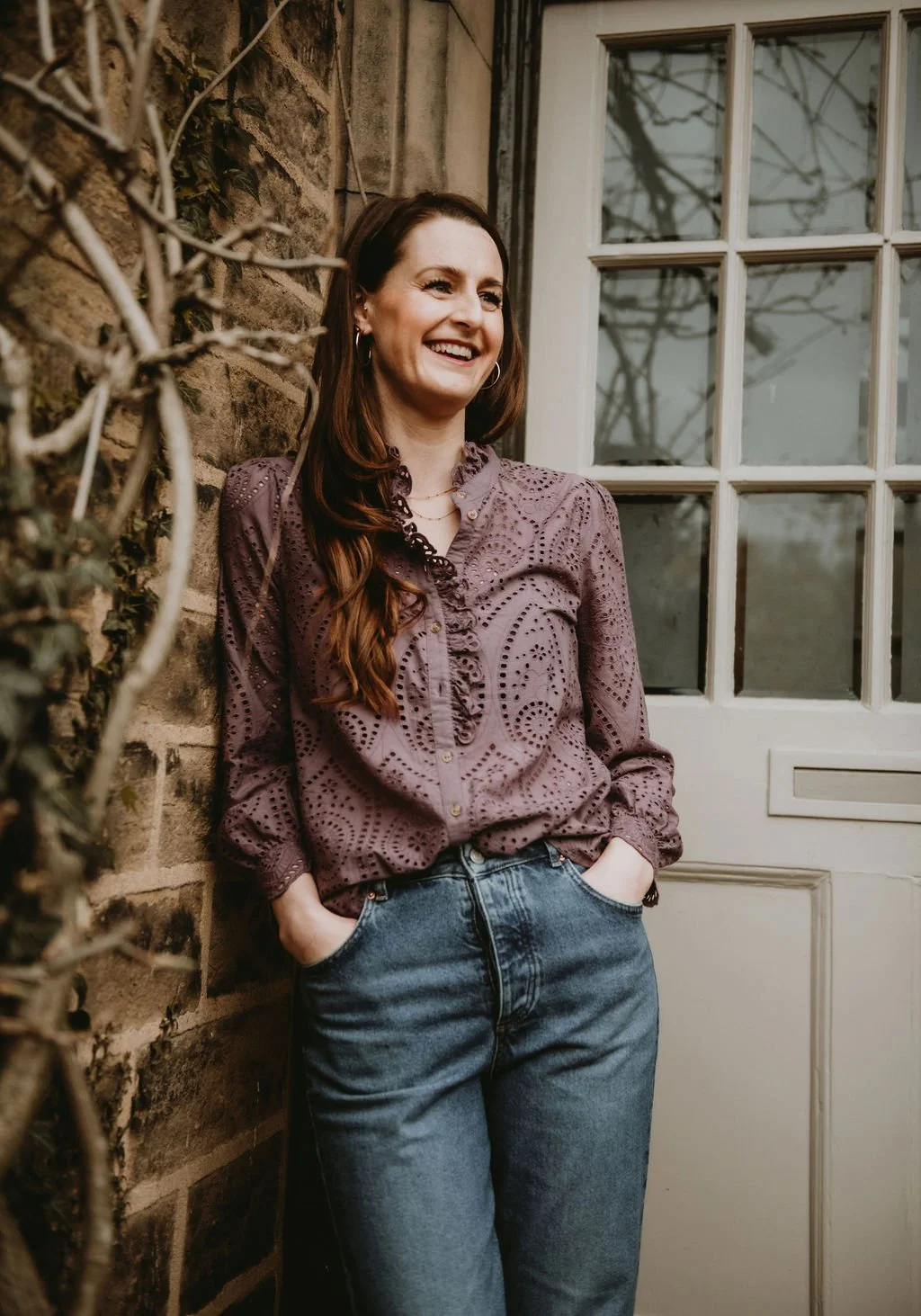 Michelle Park Celebrant stands in front of a beautiful door and against a stone wall. She wears a purple frilled shirt, holds her hands in her pockets and stares wistfully out into the distance.