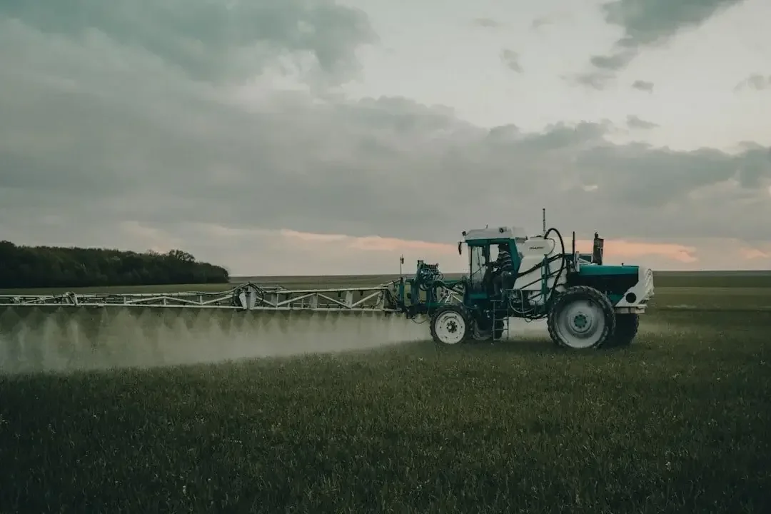 A large tractor spraying crops in a field during cloudy weather.