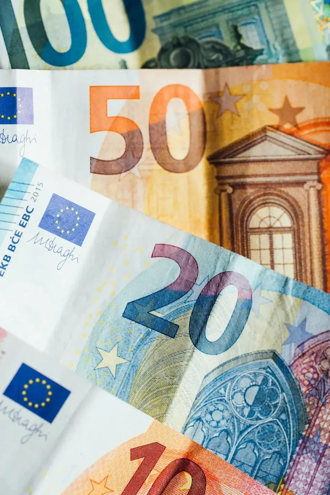 Close-up of overlapping euro bills, including a 50 euro note and a 20 euro note, showing colorful designs and architectural details.