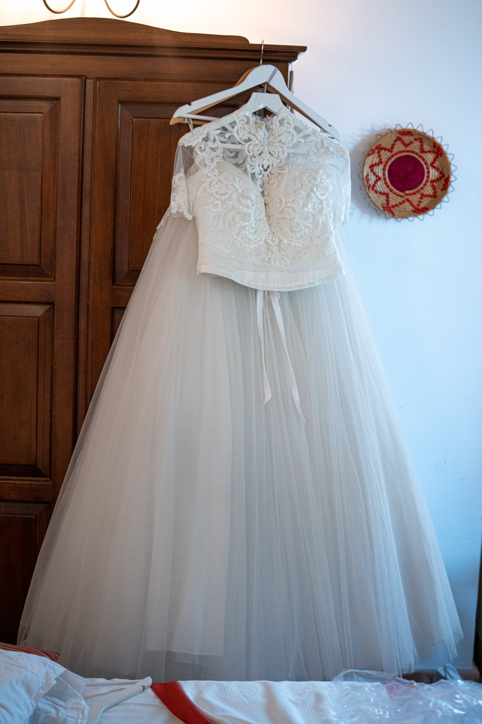 A wedding dress hanging on a hanger on a wooden wardrobe, with a lace crop top and a tulle skirt.