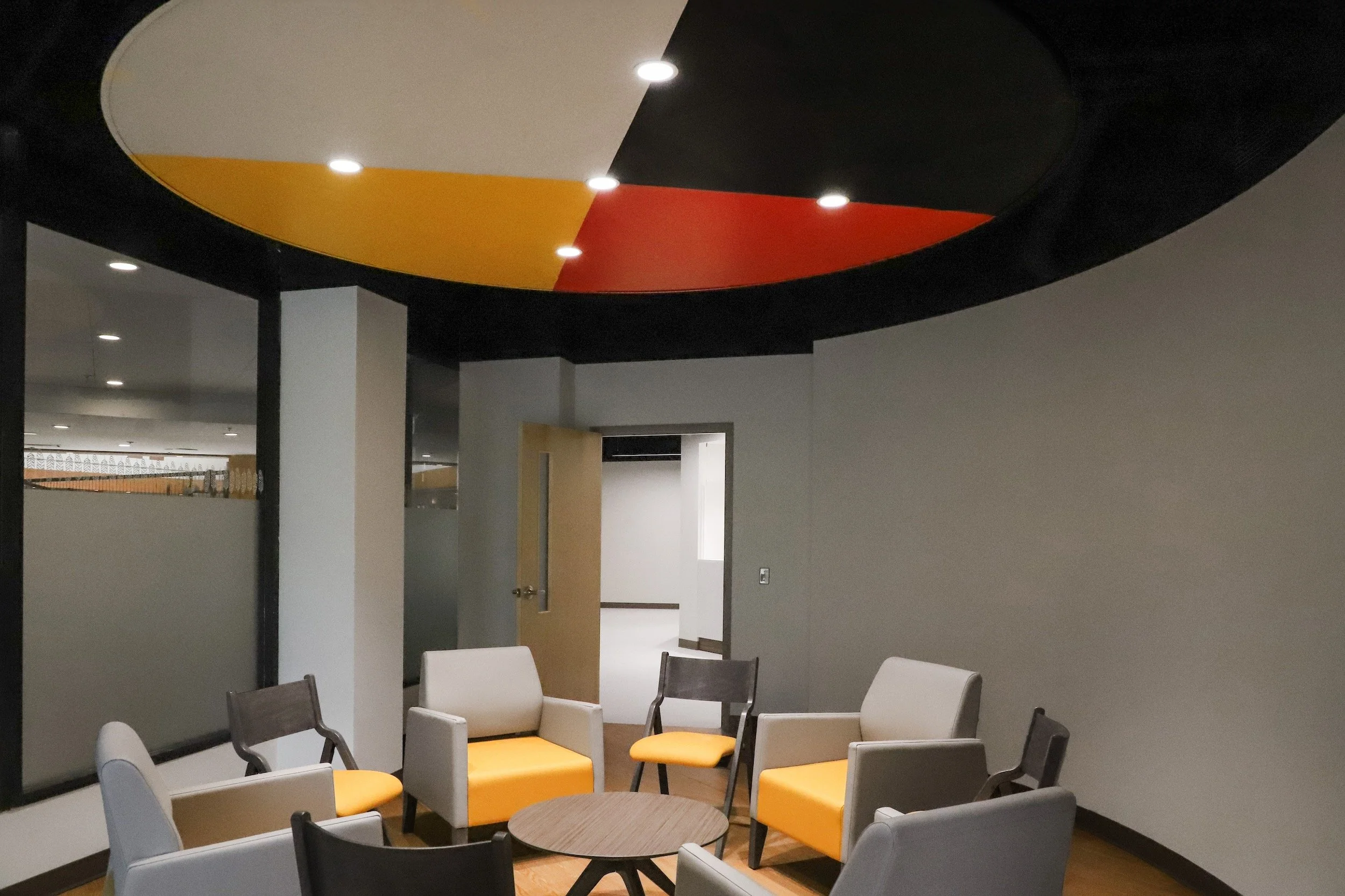 Modern office lounge with gray and white chairs around a round table beneath colorful circular ceiling panels
