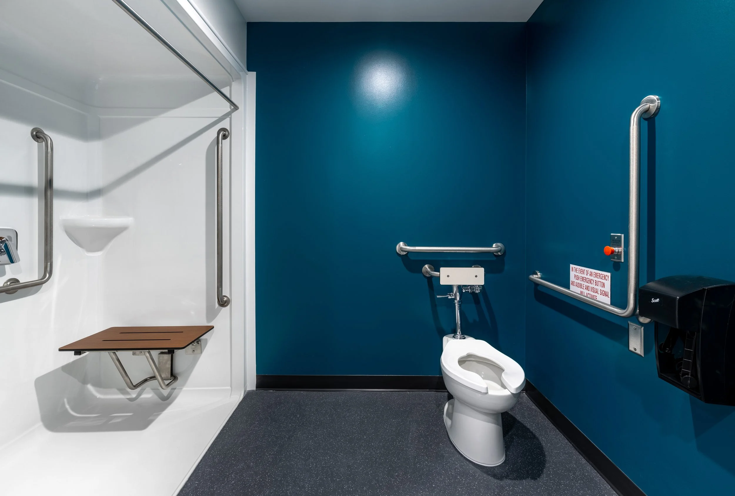A barrier free bathroom with a shower area, toilet, grab bars, and a dark blue accent wall