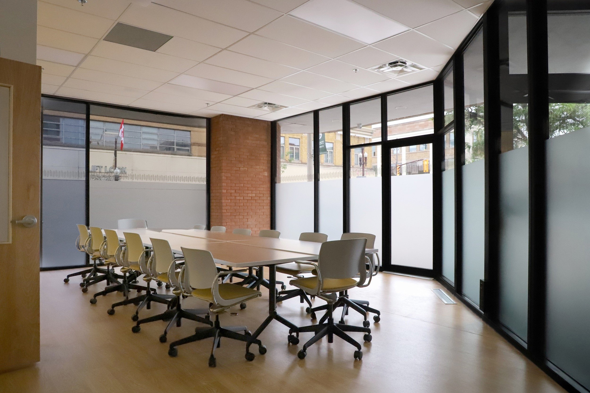 Modern conference room with a long table, rolling office chairs, glass walls, and a brick accent wall