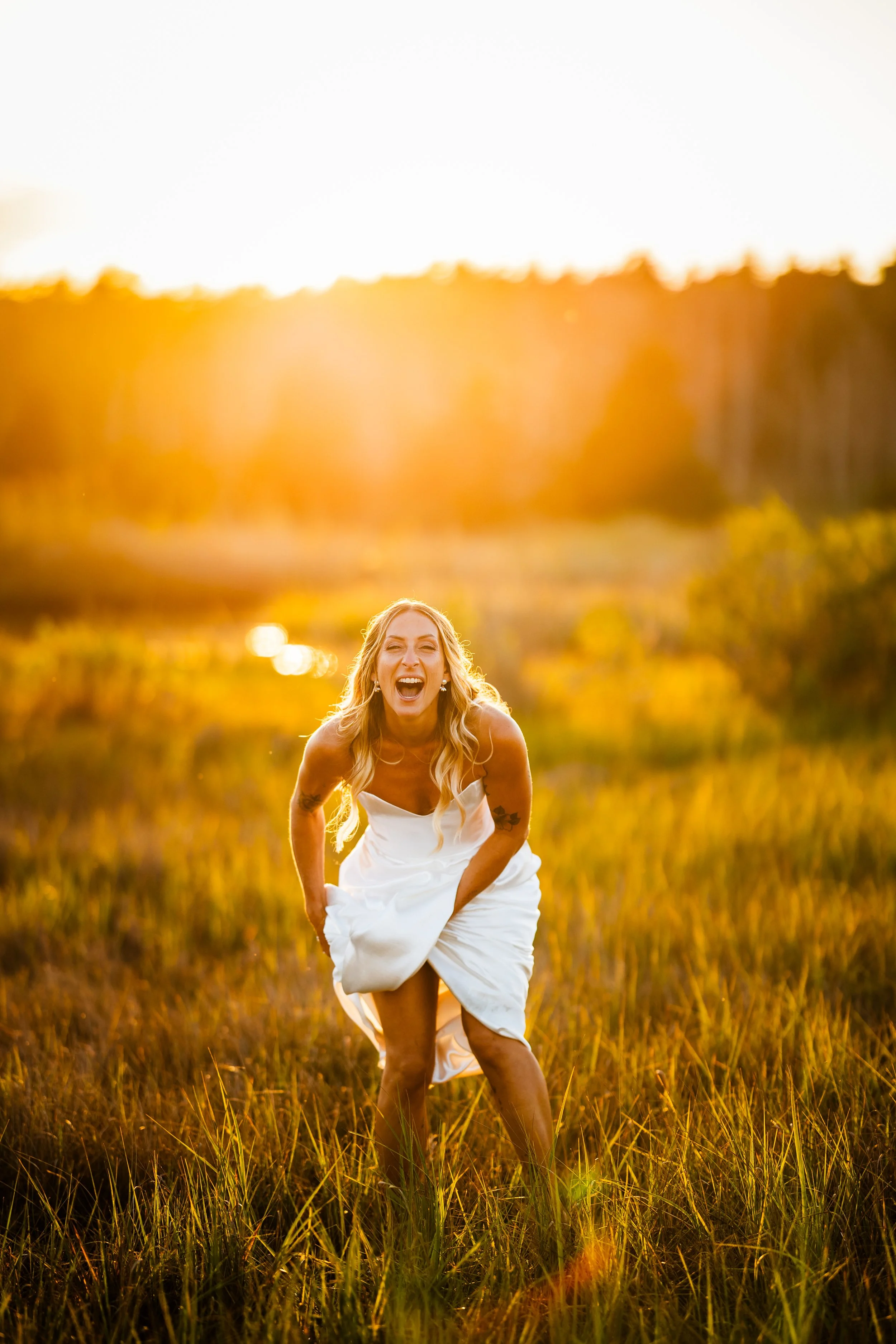 A woman in a white dress smiling and playing in a grassy field during sunset.