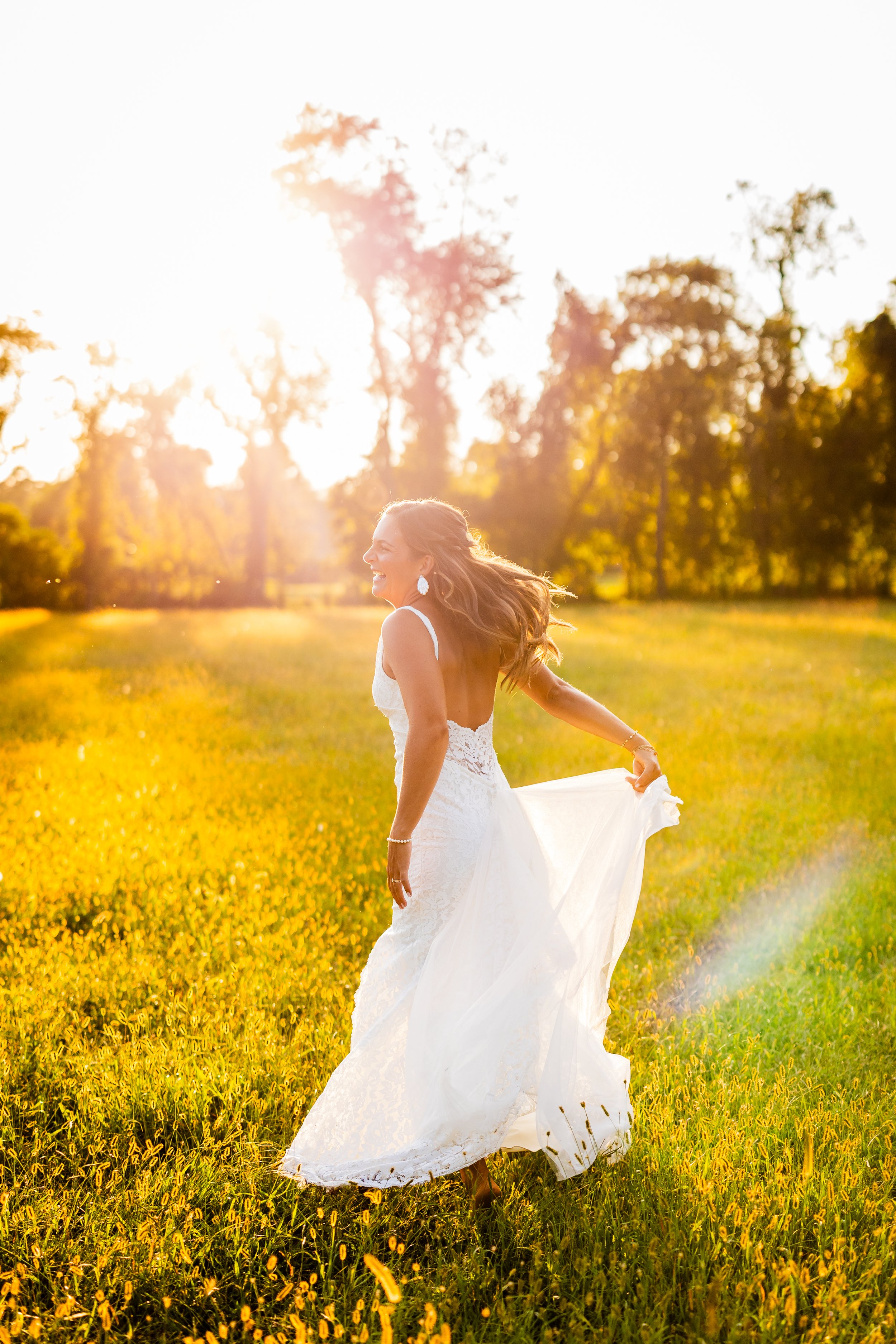 A smiling woman in a white wedding dress walking in a sunlit field during golden hour.