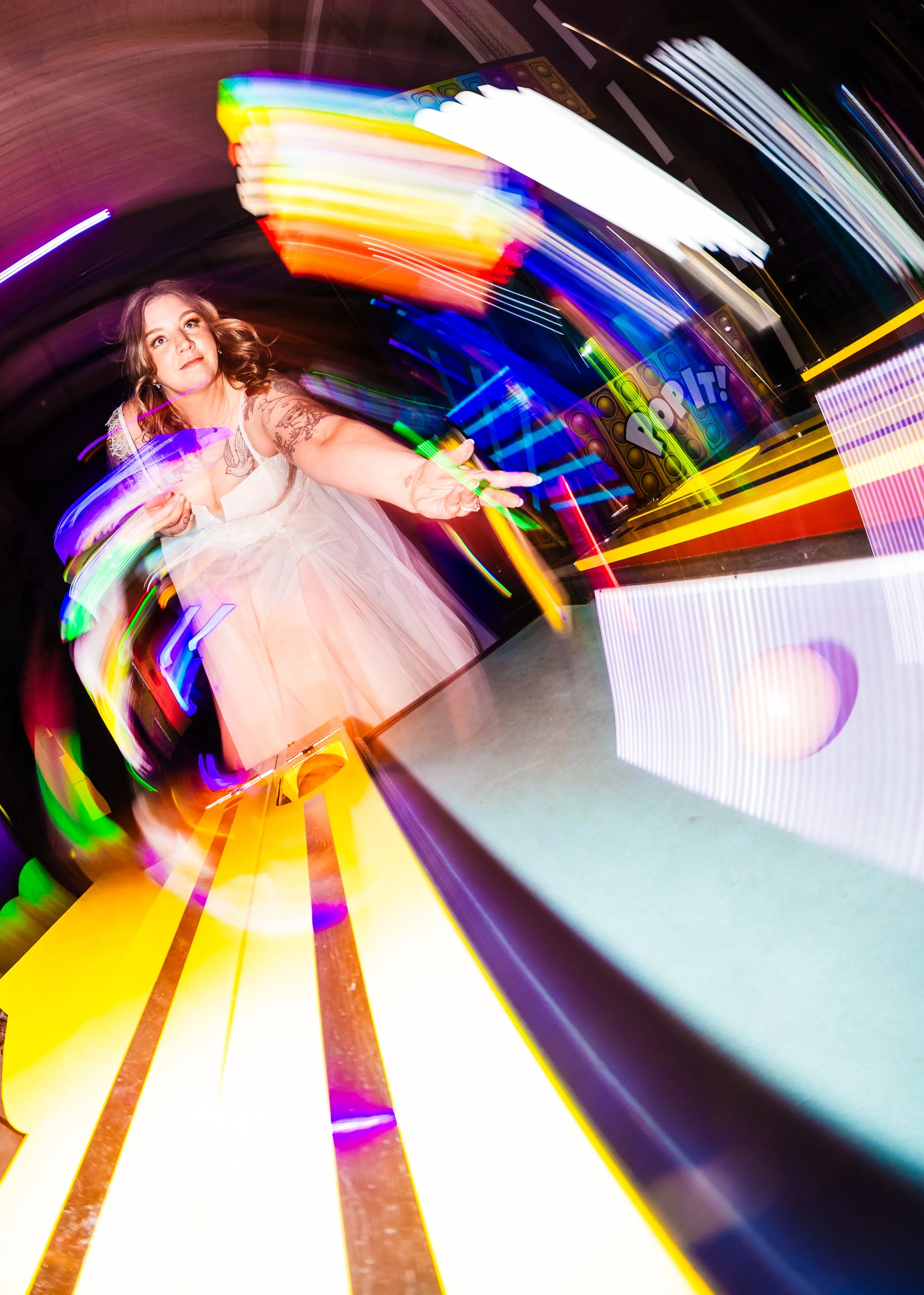 A woman in a white dress reaching out towards a colorful, blurred background with neon lights and digital displays, creating a dynamic, energetic scene.