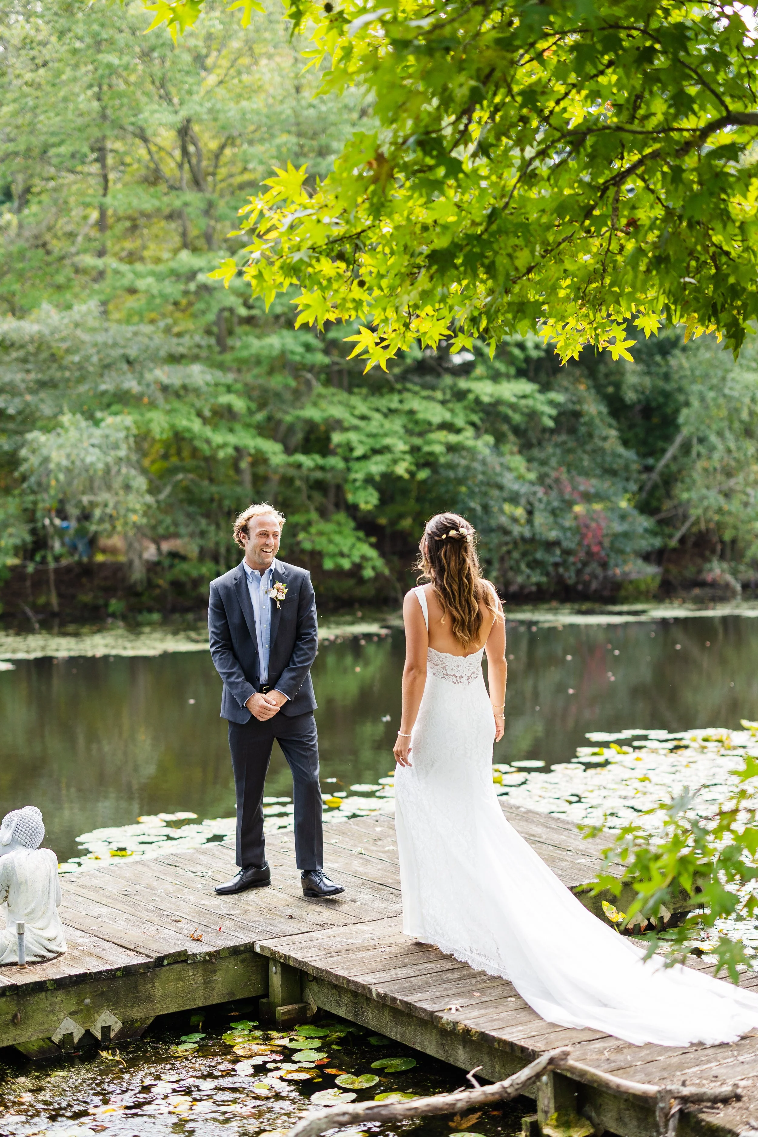 A bride and groom exchanging vows on a wooden dock by a lake surrounded by lush green trees.